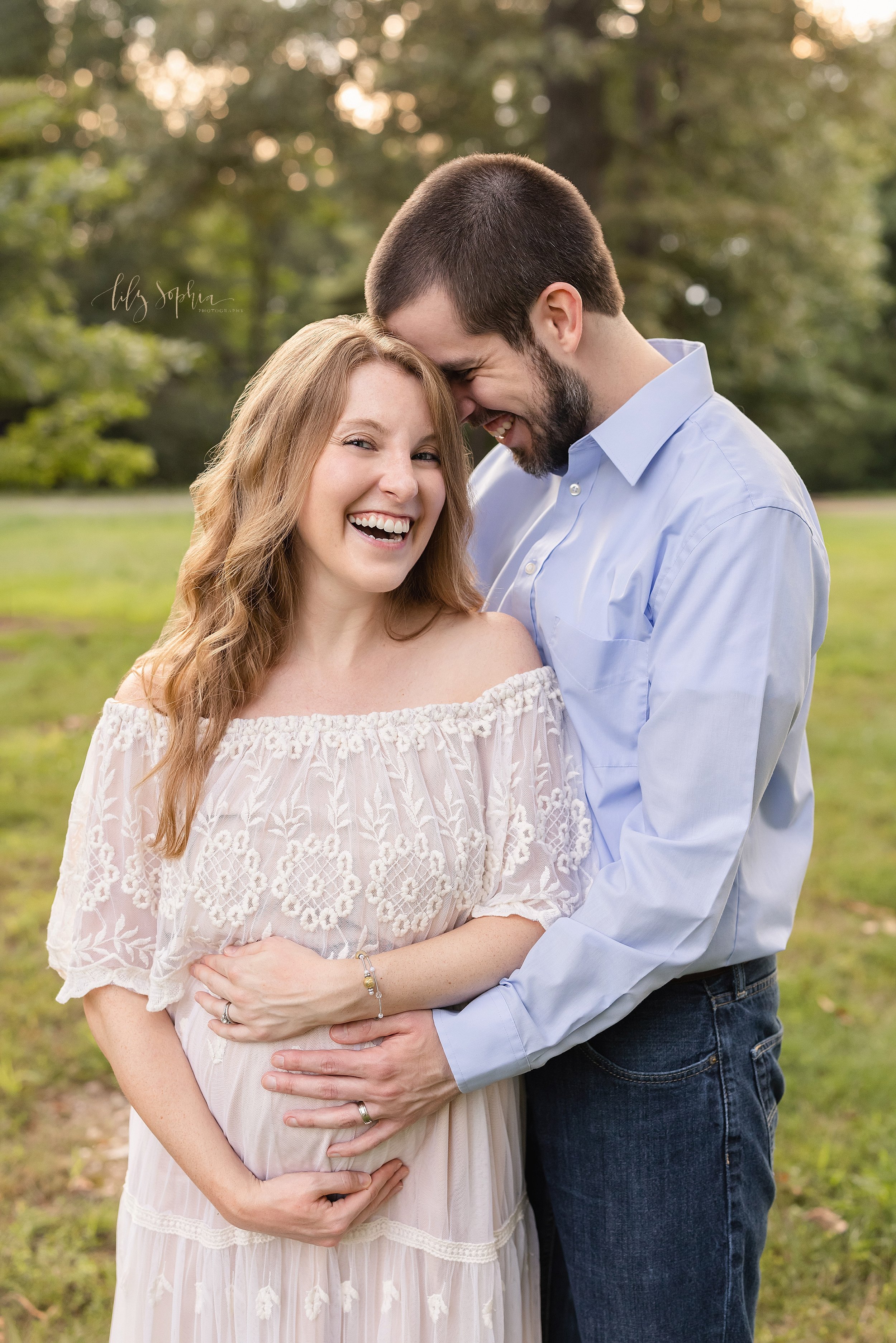  Maternity photo shoot in an Atlanta park of a pregnant mother standing in front of her husband as he places his forehead on the left side of her head while she frames her belly with her hands and he places his left hand on his child in utero as the 