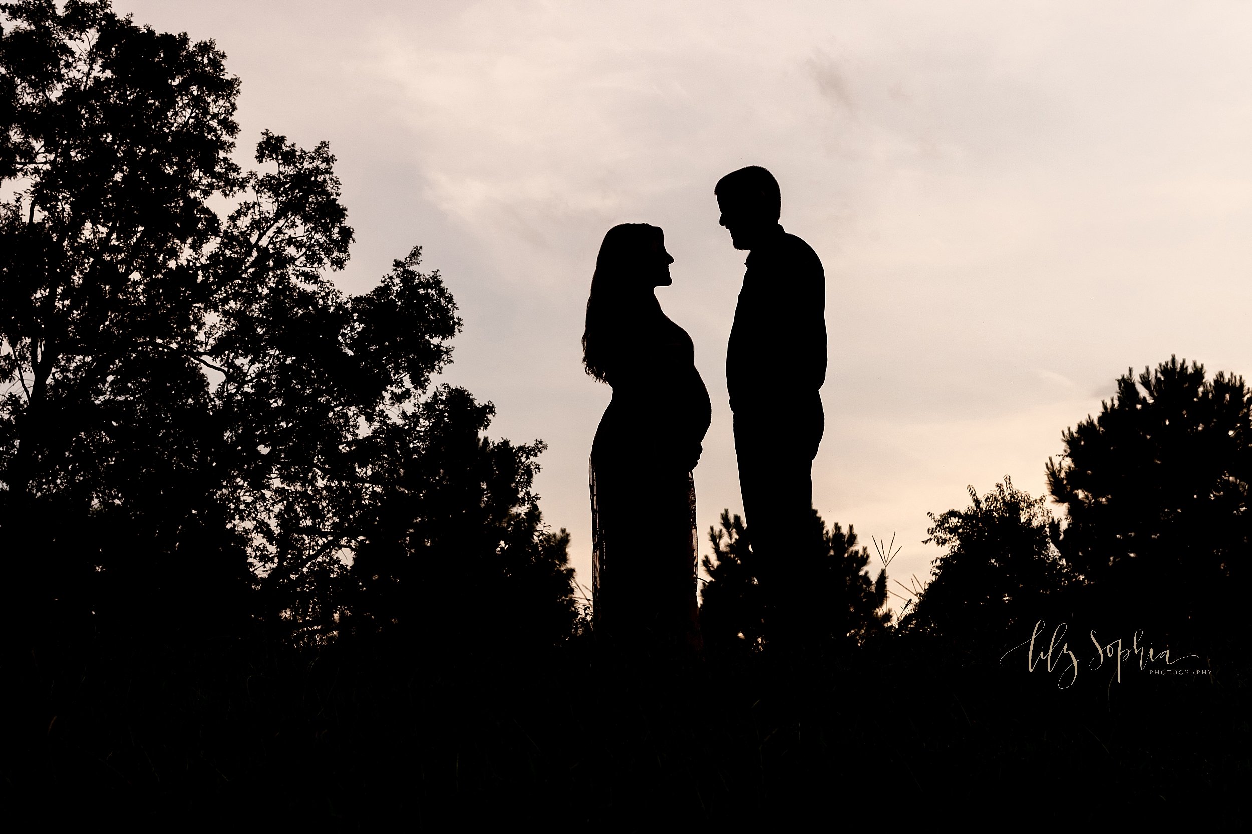  Maternity silhouette picture of a pregnant mother facing her husband taken at sunset in a field near Atlanta, Georgia. 