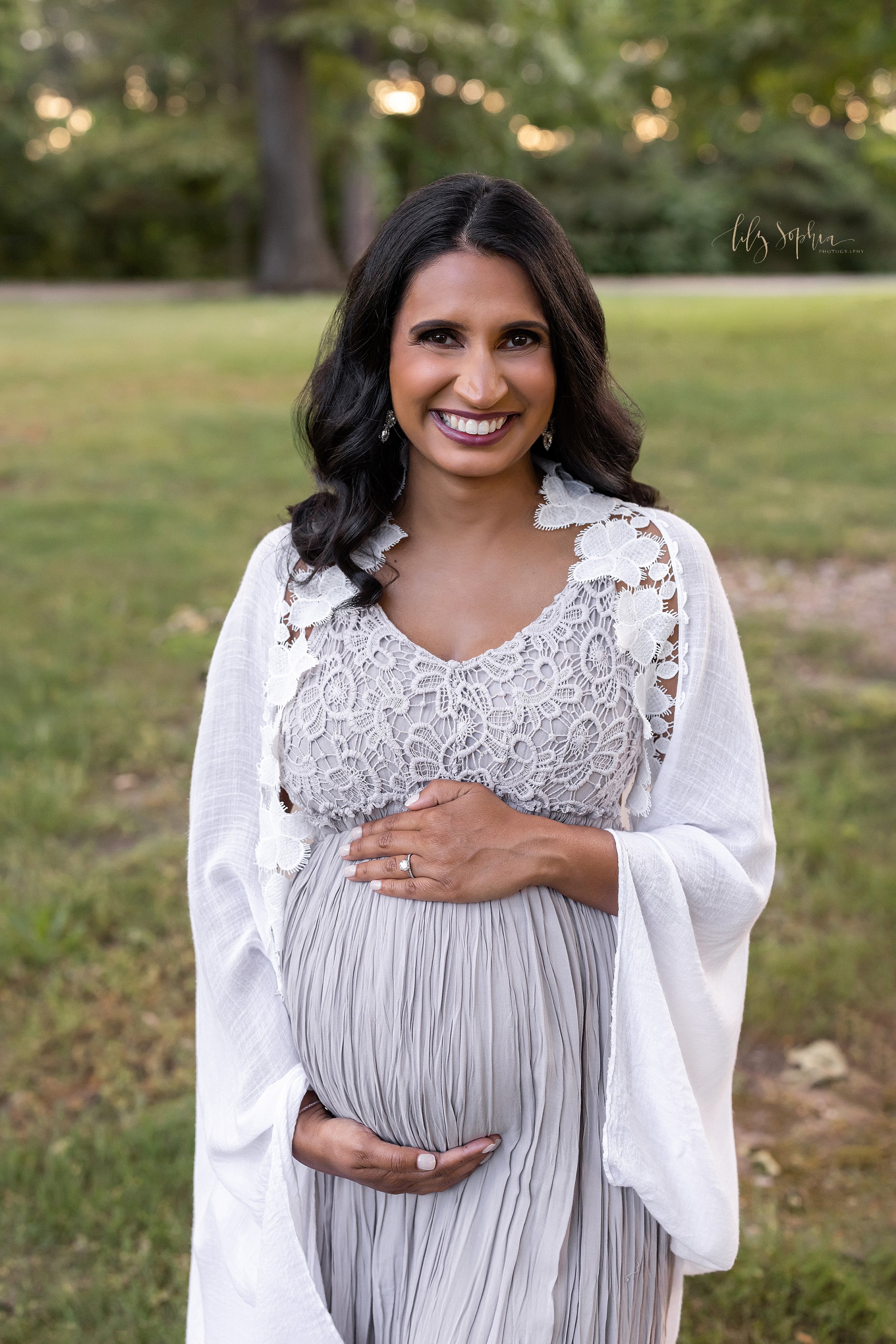  Maternity portrait of a pregnant Indian mother standing while framing her belly with her hands as the sun sets behind her in a park near Atlanta, Georgia. 