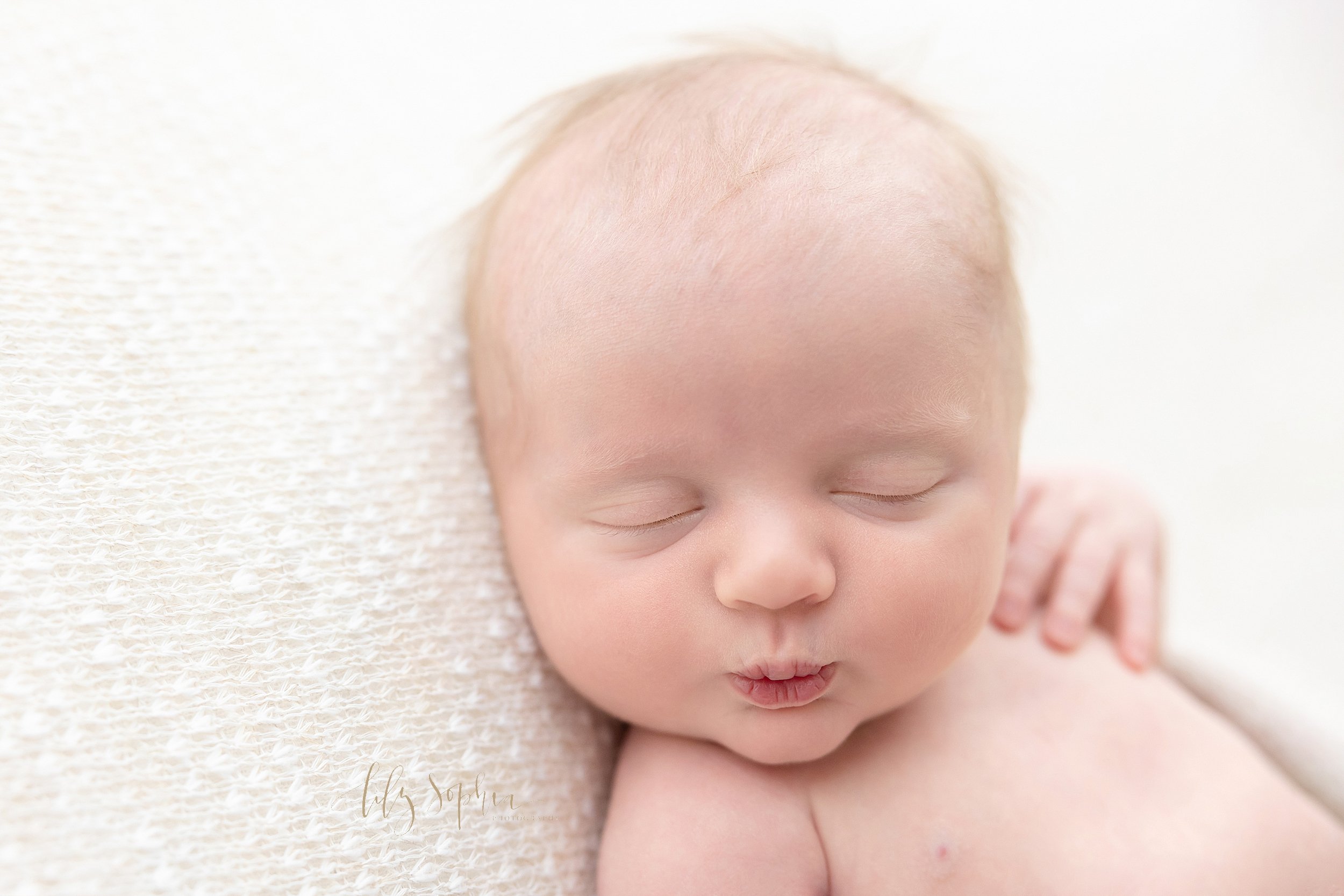  Newborn photo session in a natural light studio of a newborn baby boy as he lies on his back and puckers his lips taken near Alpharetta in Atlanta. 