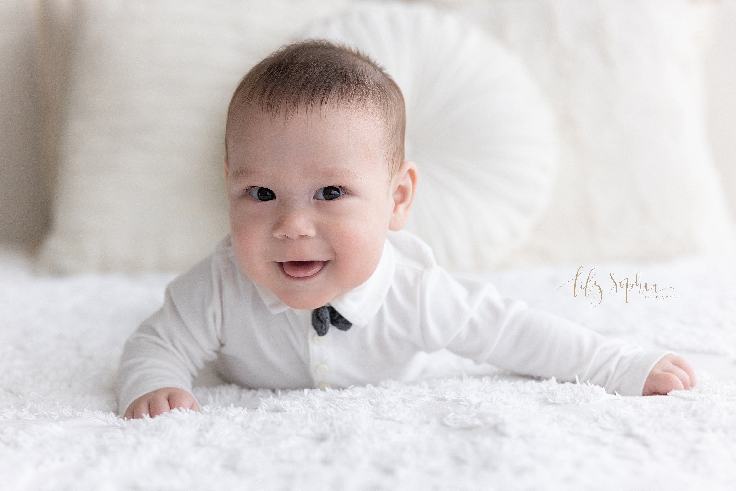 Baby photo of a baby boy as he lies on his stomach wearing a white shirt and a bow tie taken in natural light near Kirkwood in Atlanta in a photography studio. 