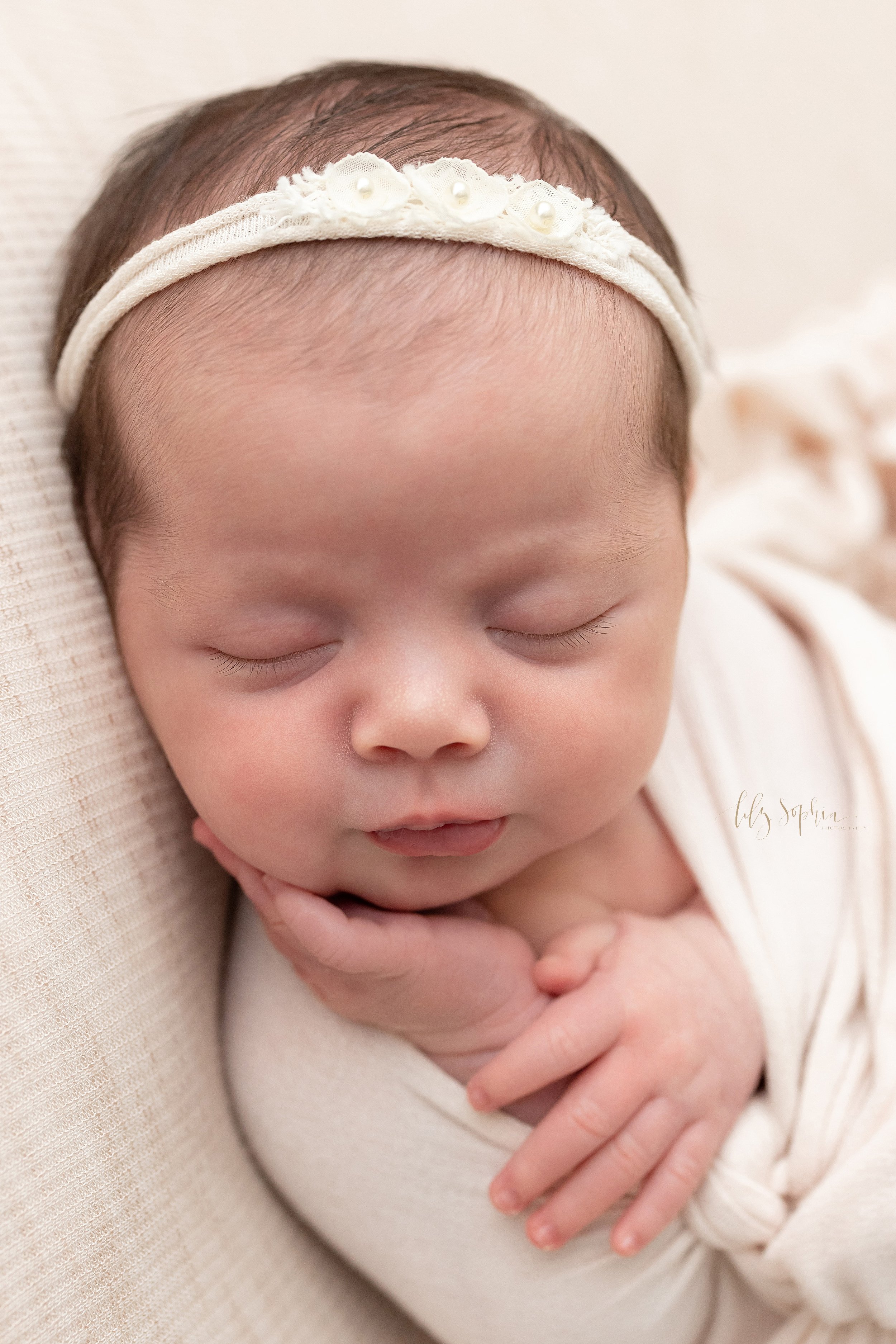  Newborn portrait of a sleeping infant girl lying on her back and turning her head over her right shoulder as she puckers her lips taken in a natural light photography studio near Buckhead in Atlanta, Georgia. 