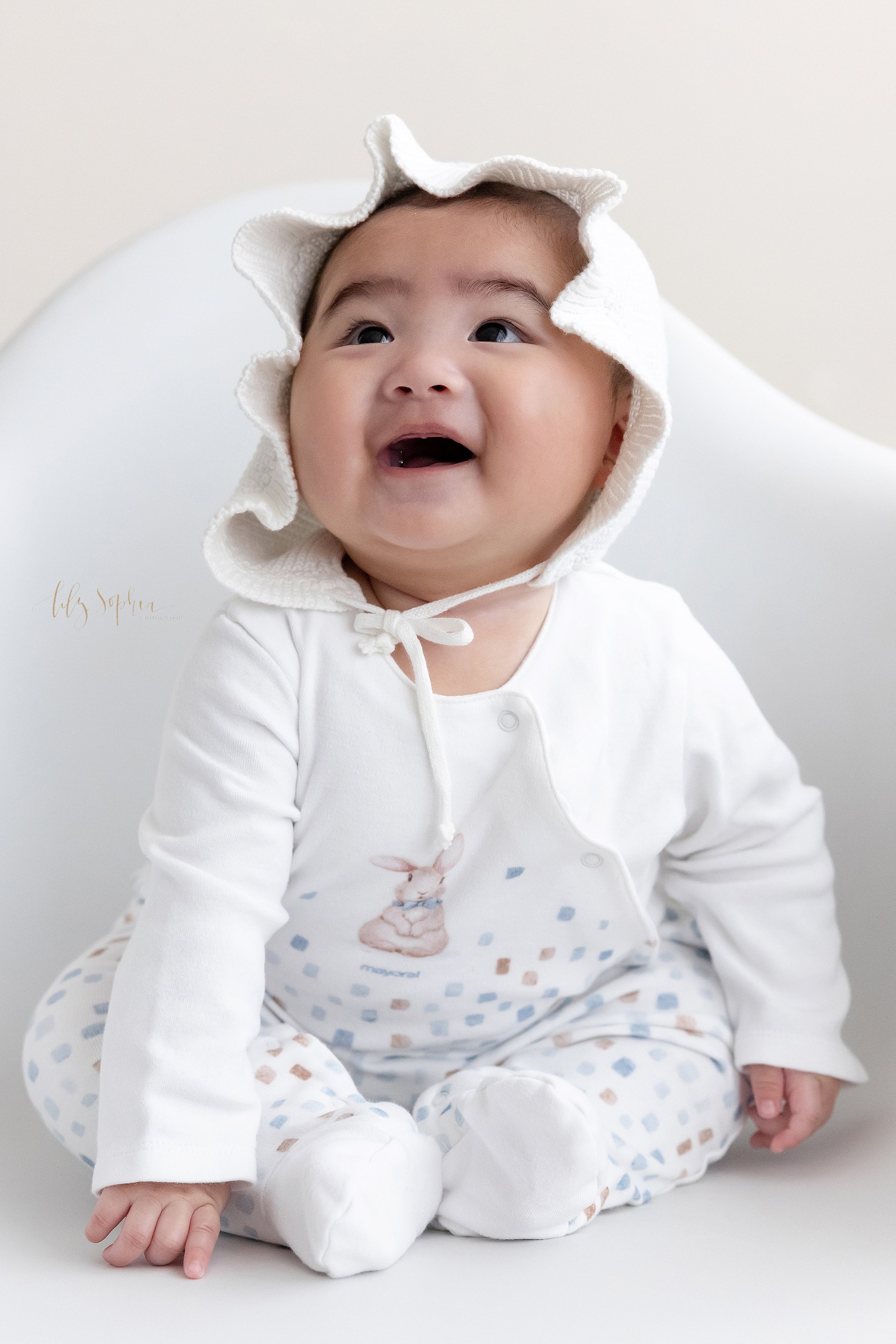  Baby photo of an Asian girl as she sits in a white molded chair and looks up to her mother taken near Smyrna in Atlanta in a studio using natural light. 