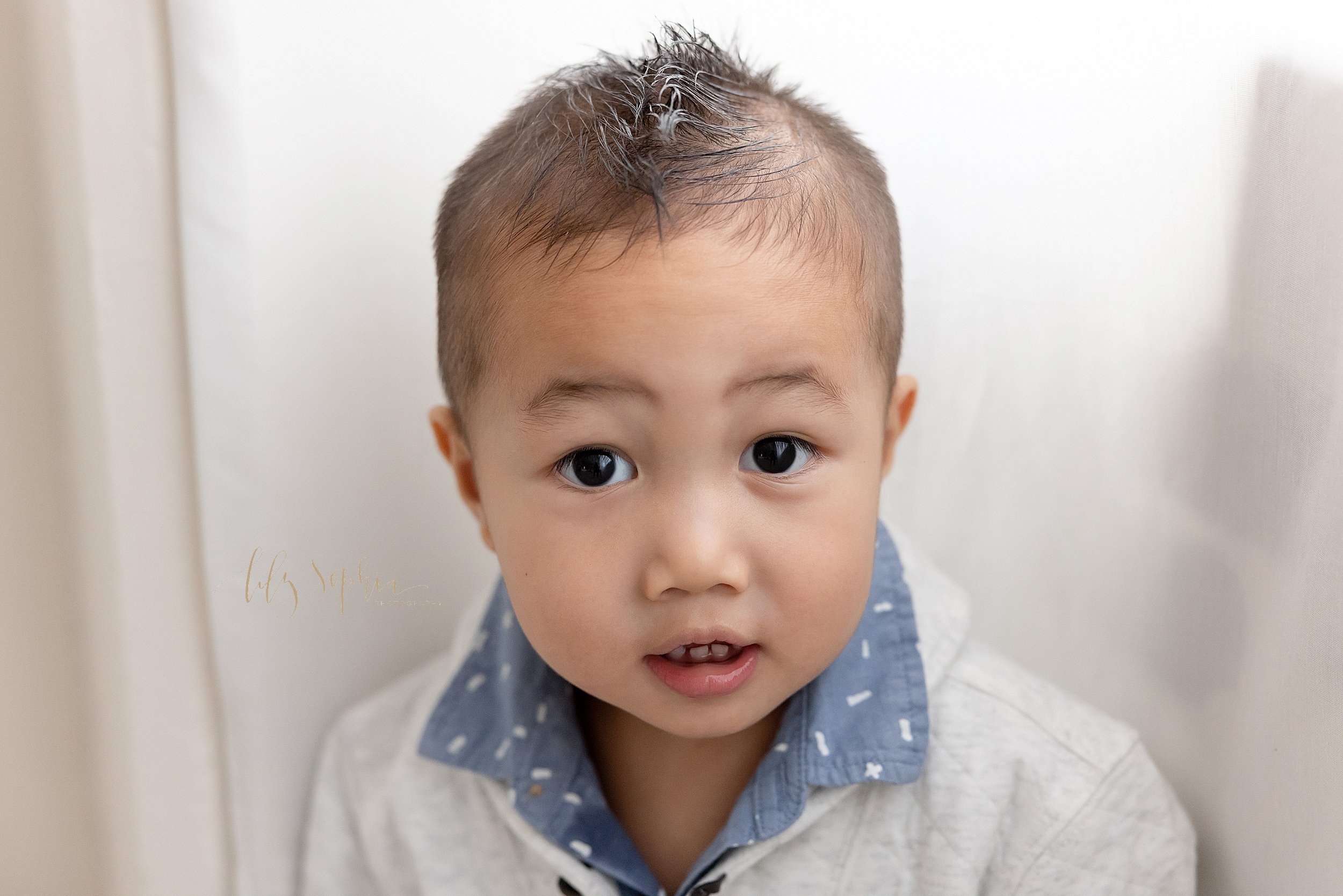  Family picture of an Asian boy as he stands in front of a window streaming natural light in a studio near Sandy Springs in Atlanta. 