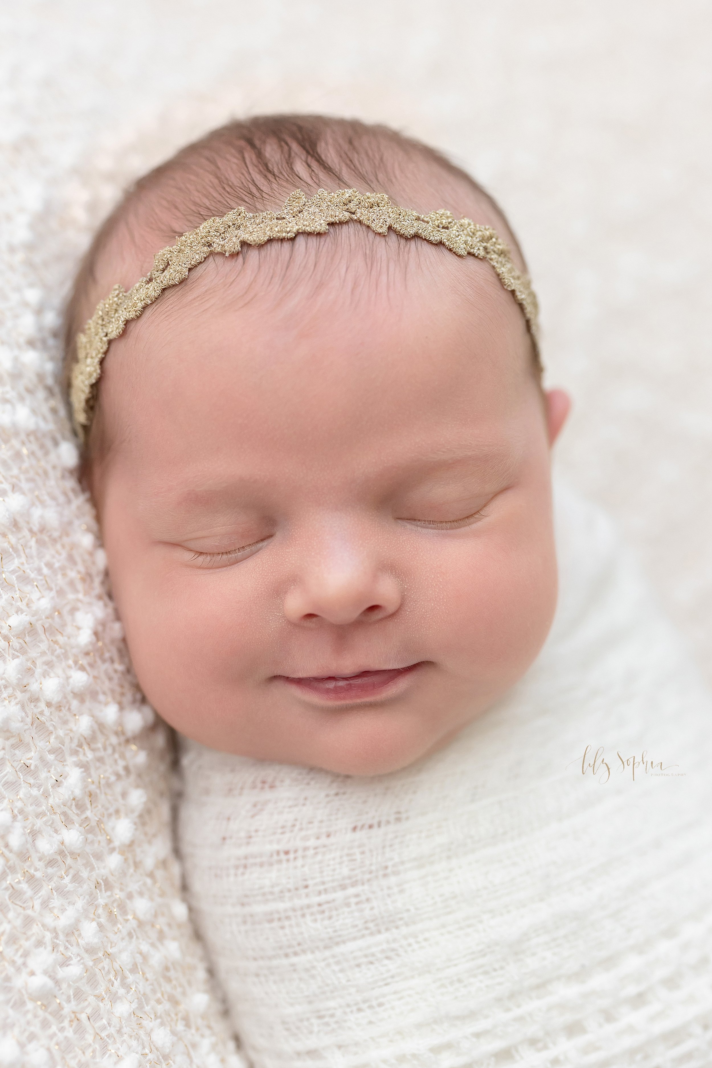  Newborn close-up portrait of a sleeping newborn baby girl as she smiles in her sleep taken in natural light near Alpharetta in Atlanta in a photography studio. 