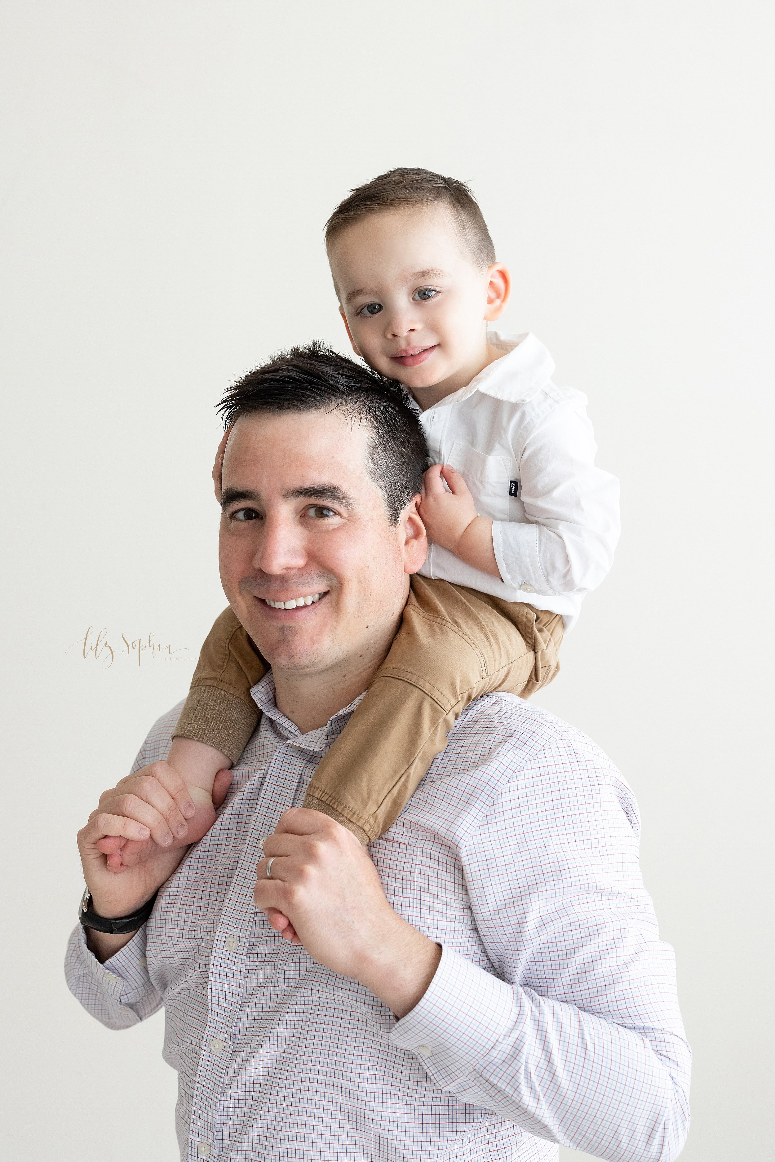  Family photo of a father riding his toddler son piggy back on his shoulders taken in a natural light studio near Midtown in Atlanta, Georgia. 