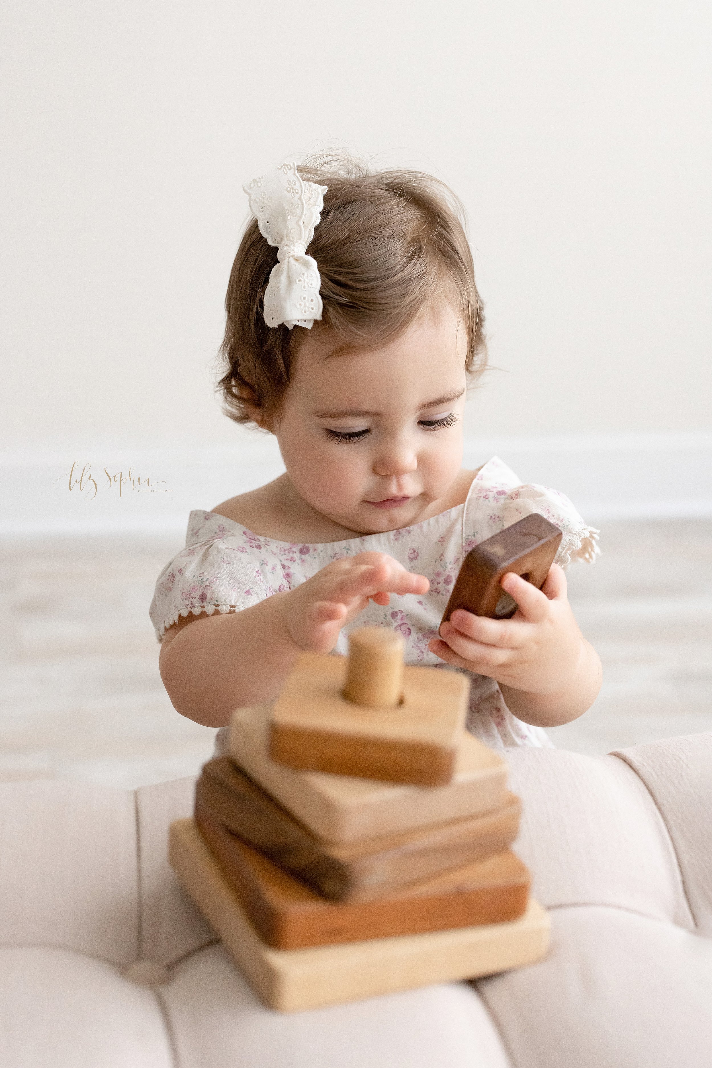  First birthday photo shoot of a one year old girl as she plays with a stacking wooden toy taken in a natural light studio near Poncey Highlands in Atlanta, Georgia. 