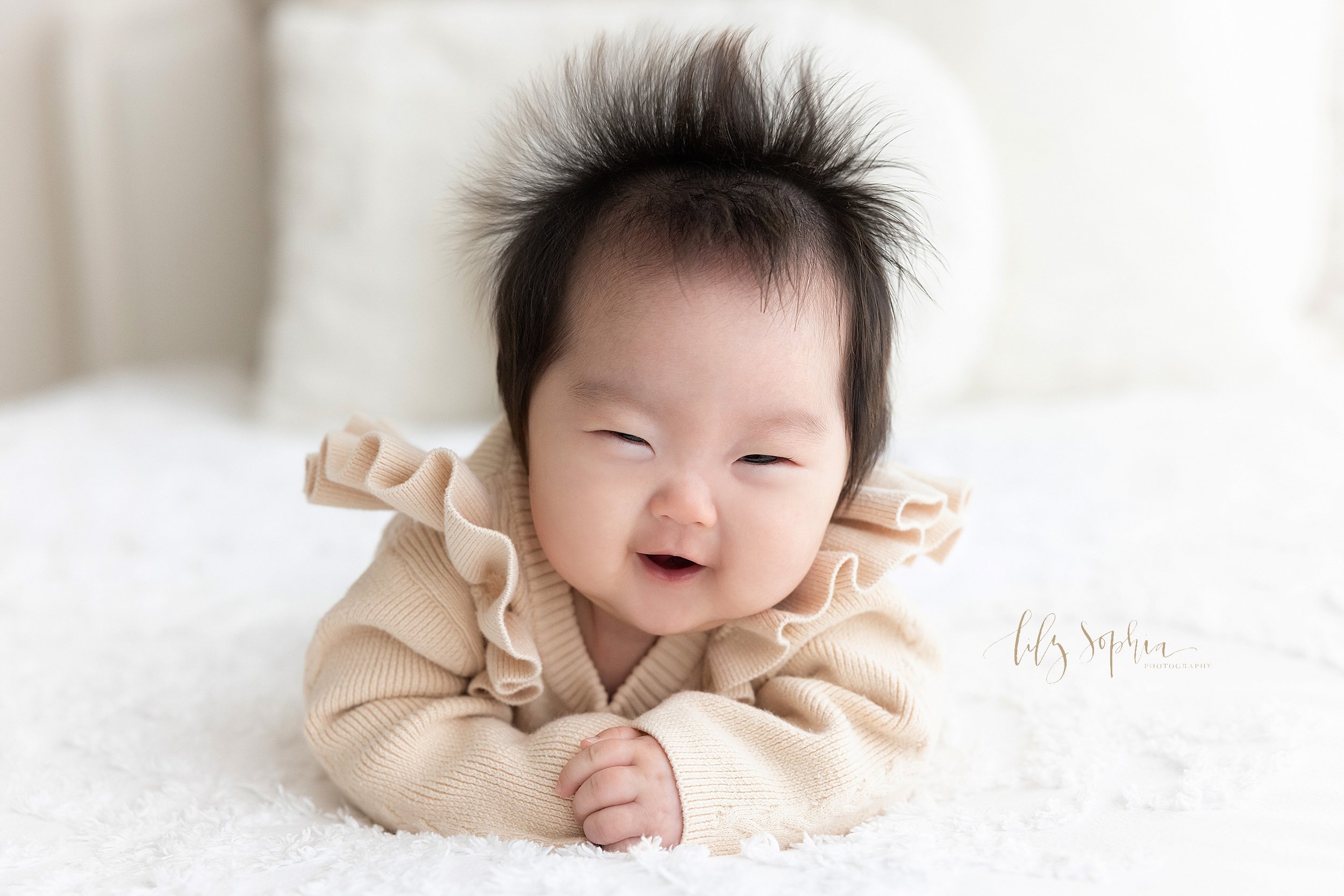  Portrait of a laughing Asian baby girl as she lies on her stomach and pushes herself up on her elbows taken in a natural light studio near Decatur in Atlanta. 