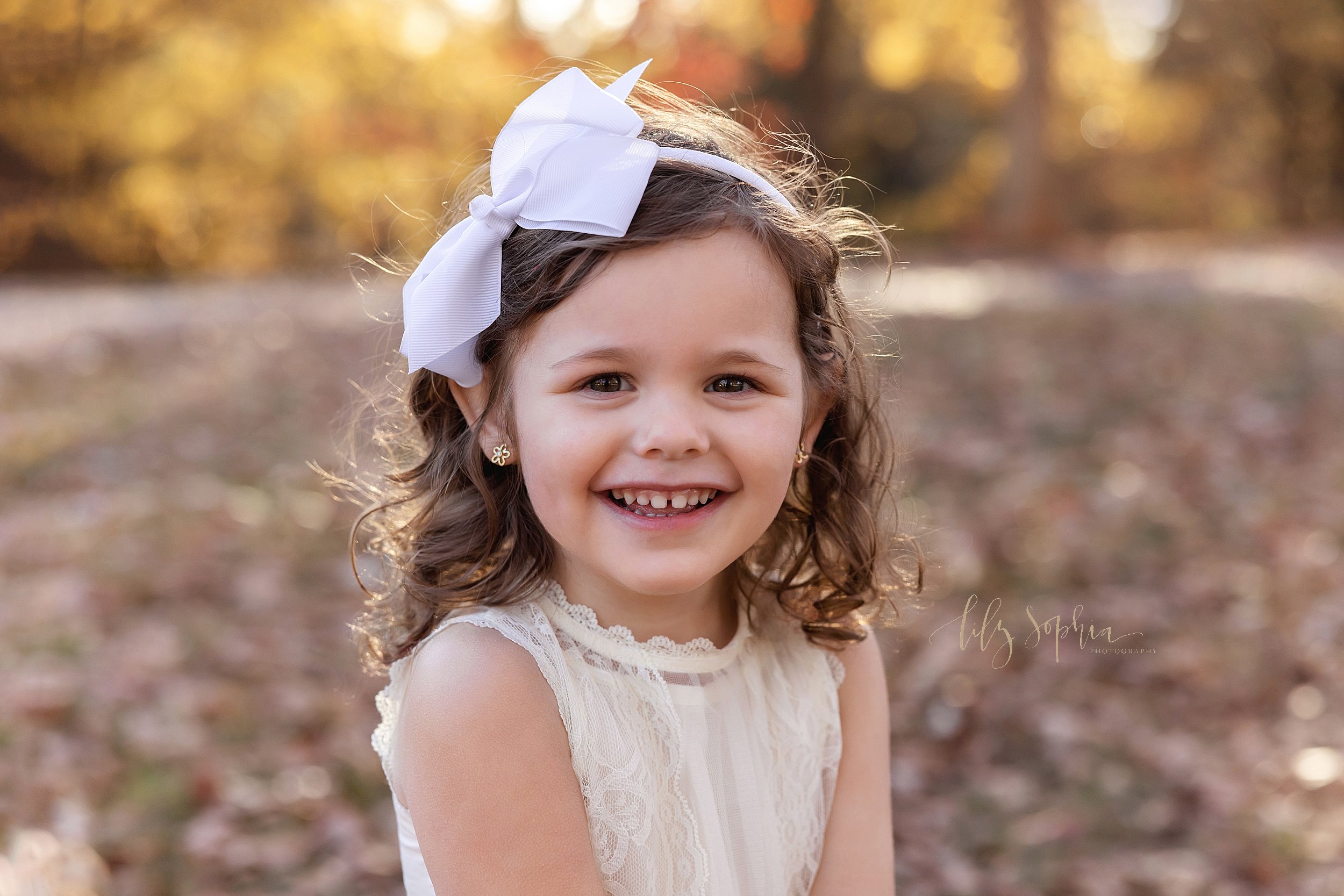  Close-up family picture of a young girl wearing a headband with a large white bow on it at sunset during autumn in a park near Atlanta. 