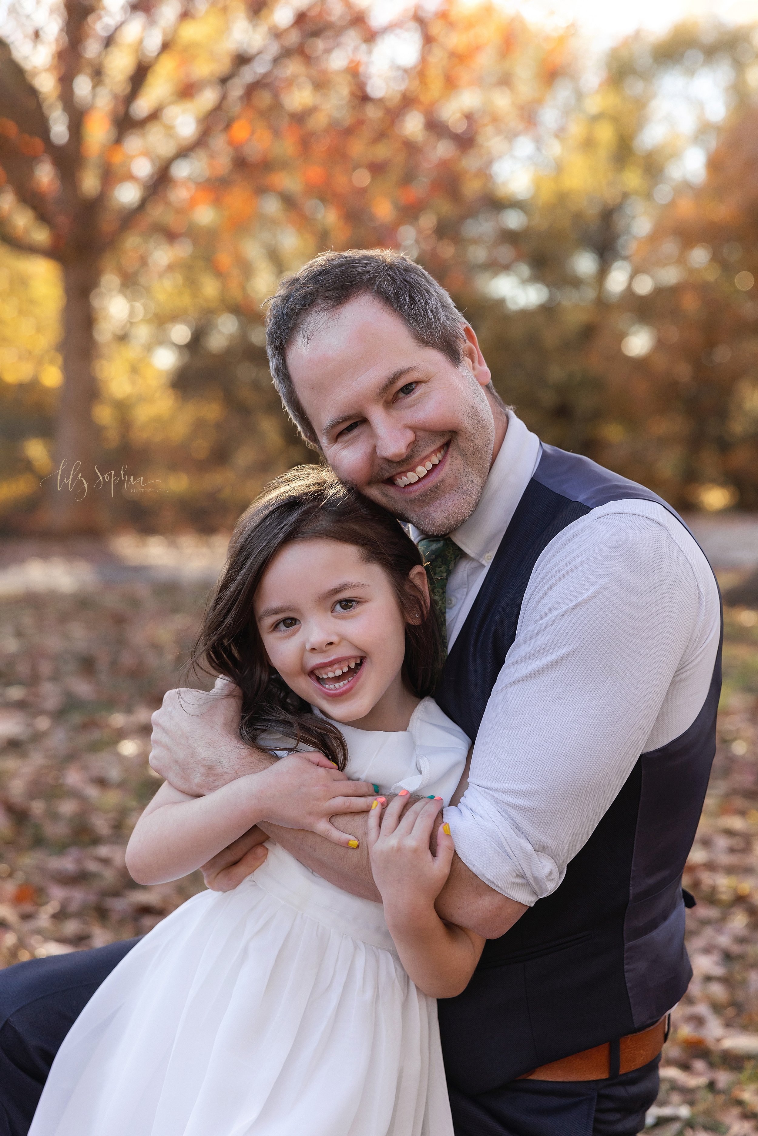 Family photo session with a father and his young daughter as he hugs her while kneeling in a park near Atlanta during autumn at sunset. 