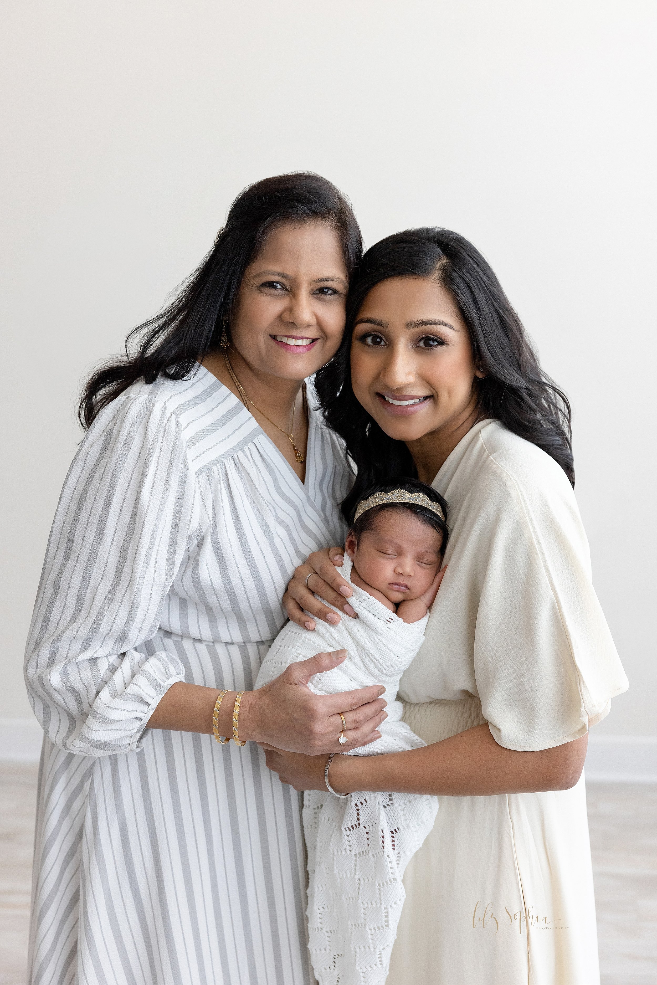  Family generational photo of a mother holding her newborn baby girl in her arms as her mother stands beside her taken in a photography studio near Poncey Highlands in Atlanta that uses natural light. 