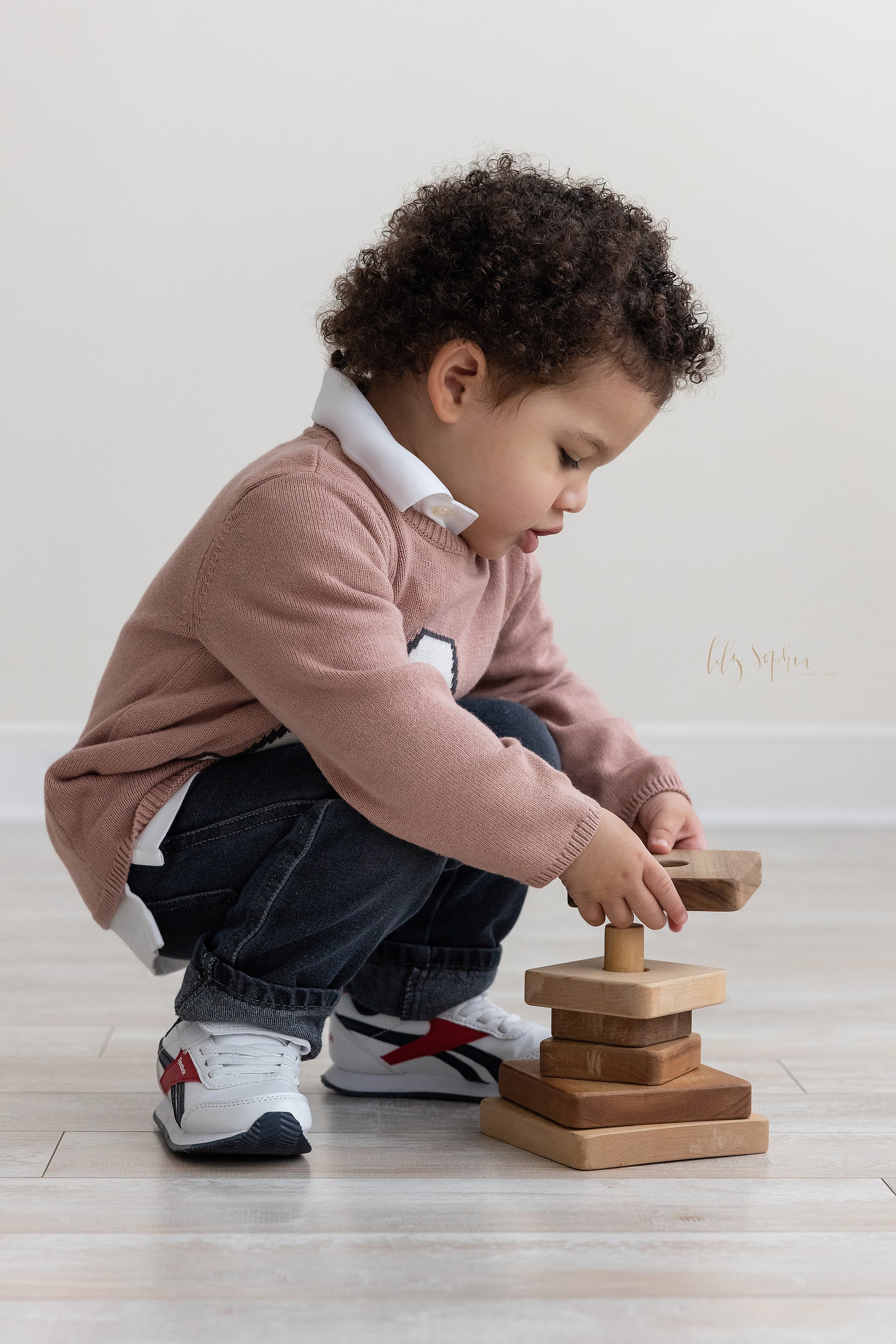  Milestone photo of a two year old boy as he squats to place a piece on a wooden stacking toy in a natural light studio near Old Fourth Ward in Atlanta, Georgia. 