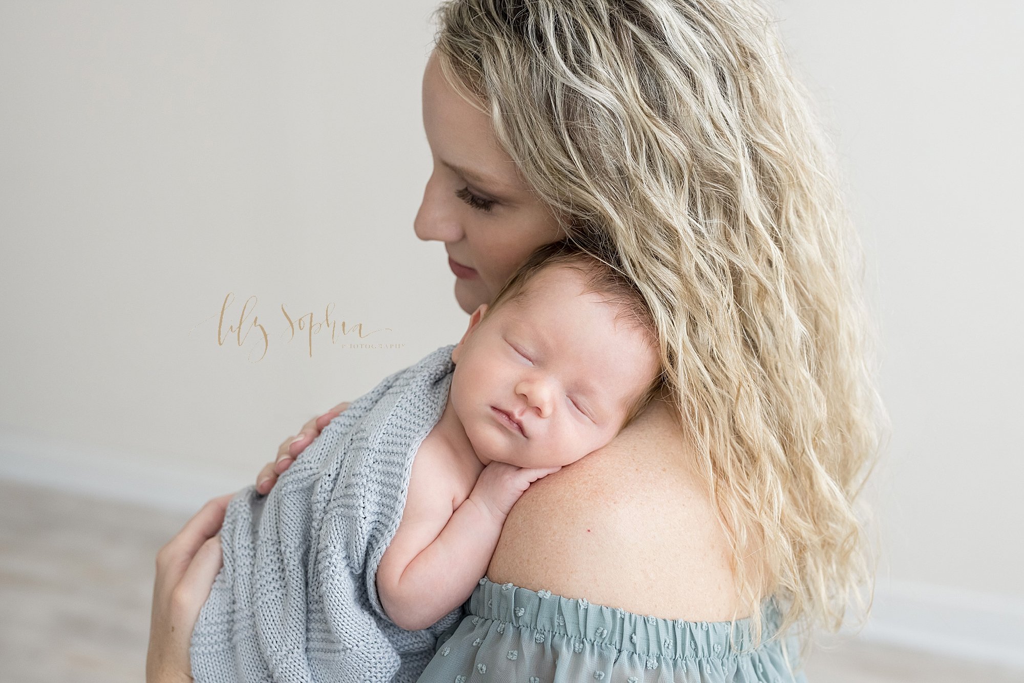  Newborn portrait of a proud mother as she holds her peacefully sleeping newborn baby boy on her shoulder as she stands in a studio that uses natural light near Brookhaven in Atlanta, Georgia. 