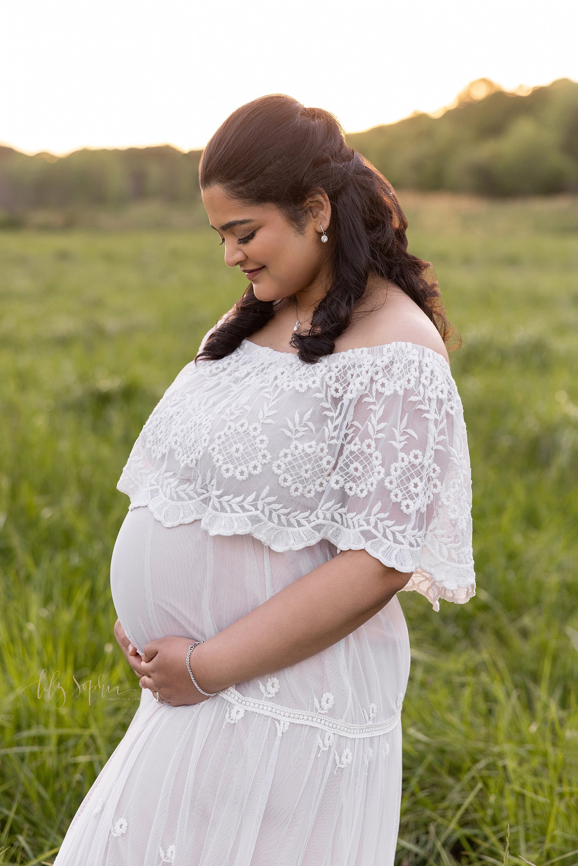  Maternity portrait of a pregnant mother as she stands facing the left and holding the base of her belly in at sunset in an Atlanta field. 