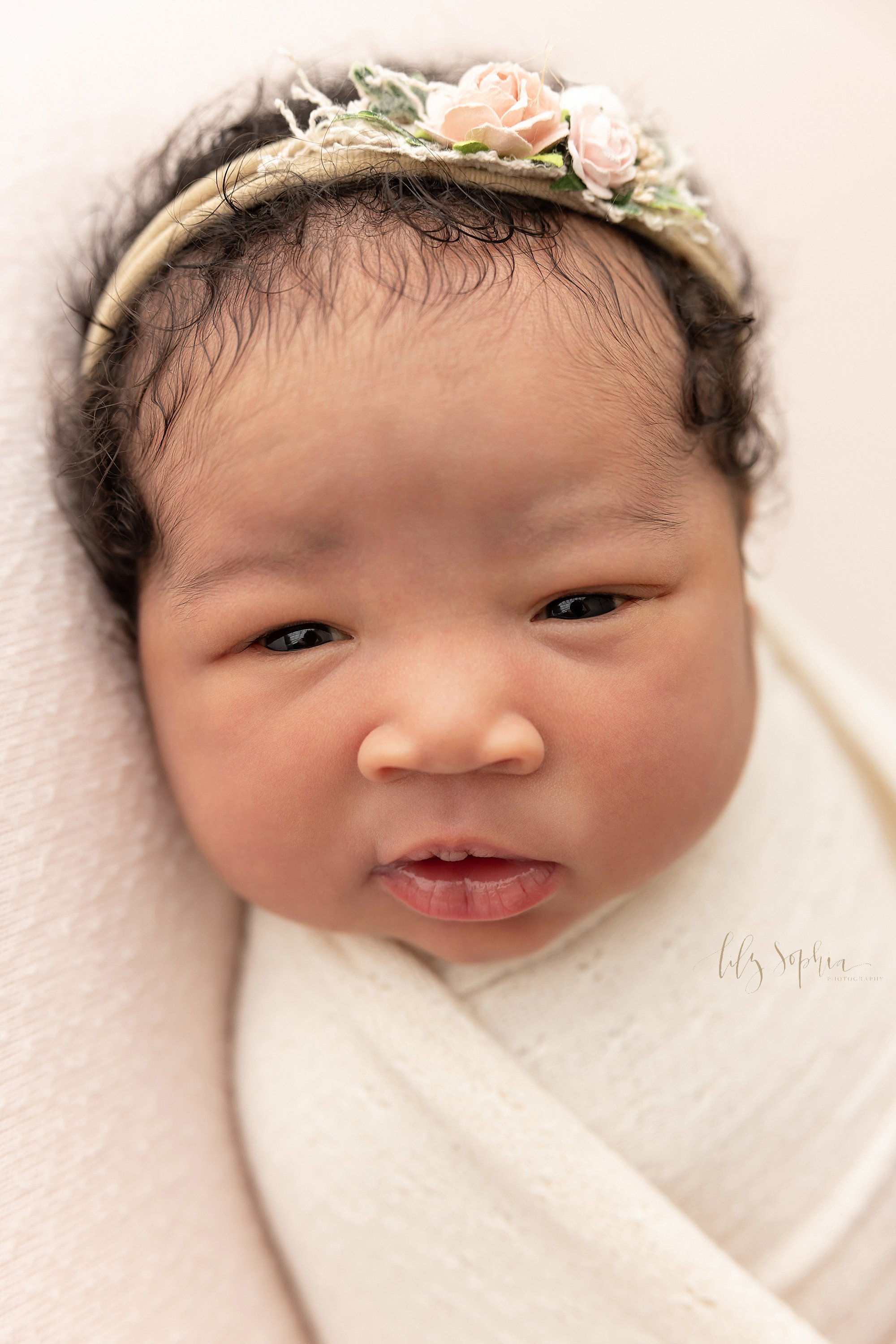  Close-up newborn portrait of an awake African-American baby girl swaddled to her chin in a soft white cloth taken in a studio near Vinings in Atlanta that uses natural light. 