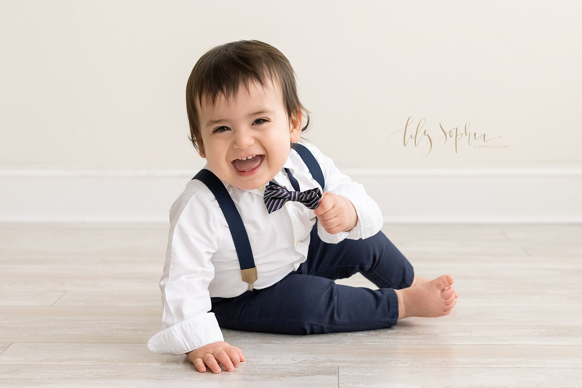  First birthday portrait of a one year old little boy as he leans on his right hand while sitting on the floor of a natural light studio near Midtown in Atlanta, Georgia. 