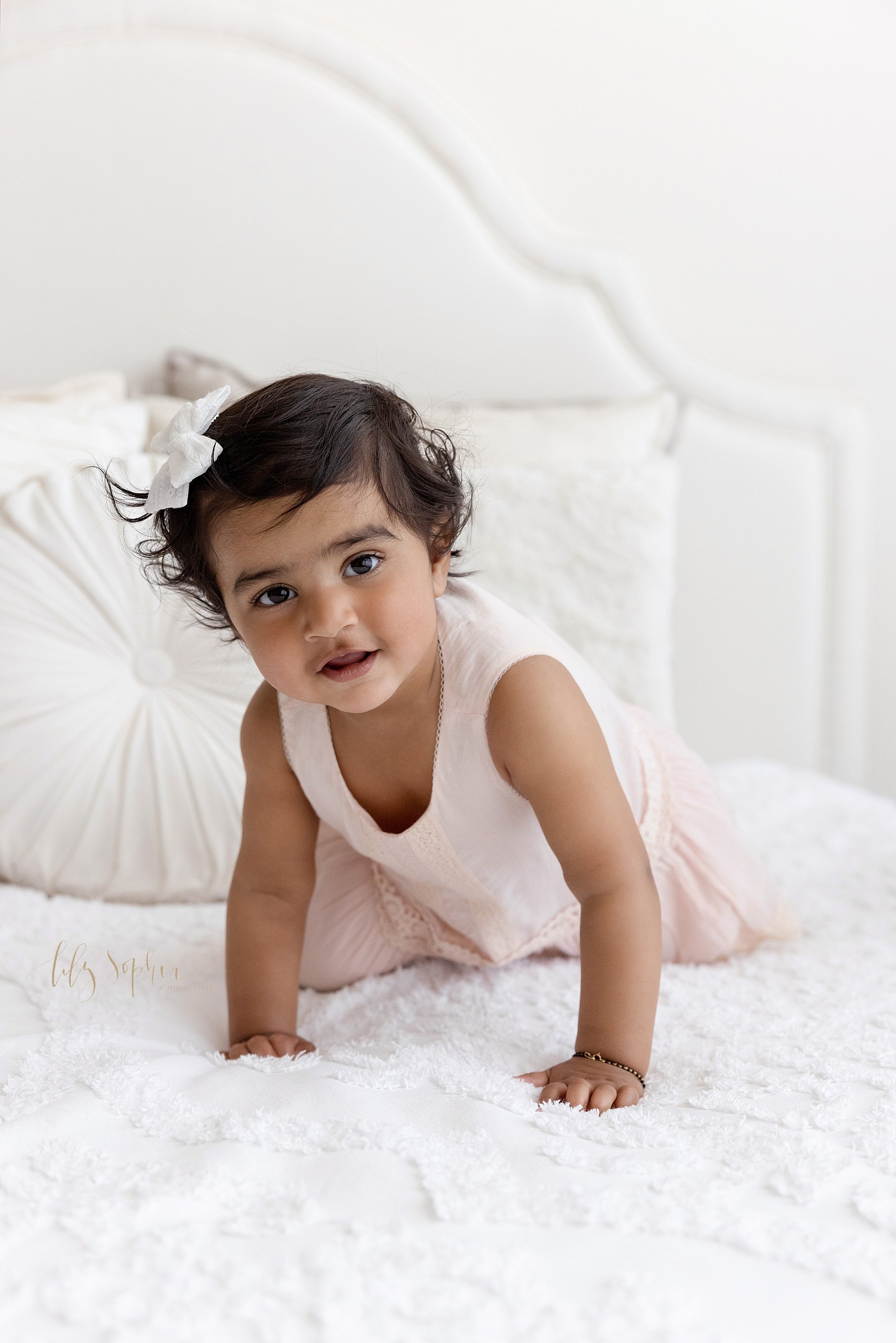  First birthday photo of a one year old little girl as she crawls across the top of a bed in a studio near Kirkwood in Atlanta using natural light. 
