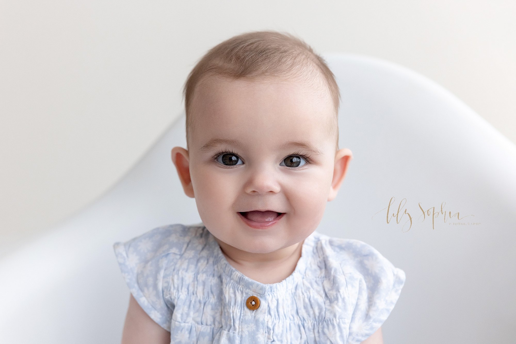  Close-up picture of a happy baby girl as she sits in a white molded chair taken near Kirkwood in Atlanta, Georgia in a studio that uses natural light. 