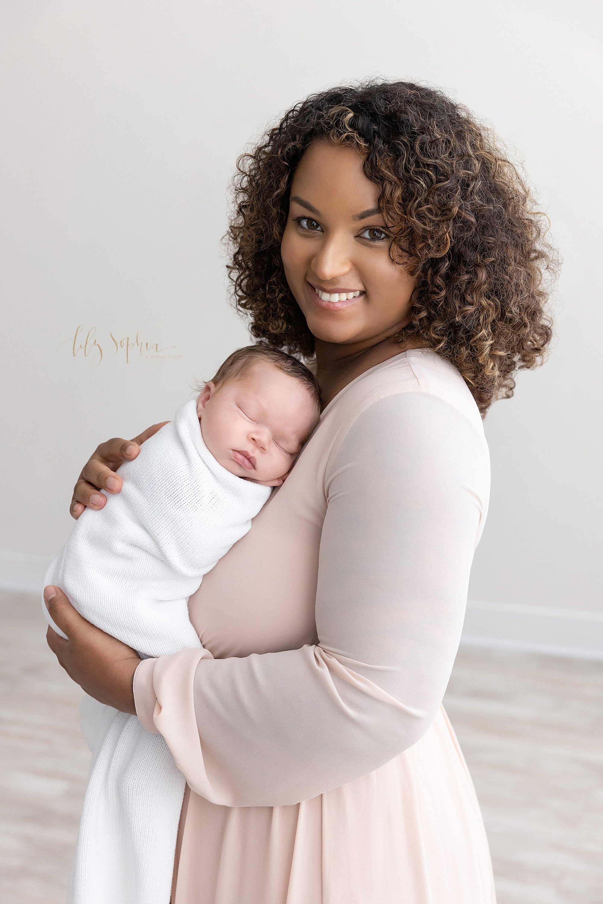 Newborn portrait of an African-American mother holding her peacefully sleeping newborn baby boy against her chest as she stands in a natural light studio near Midtown in Atlanta. 
