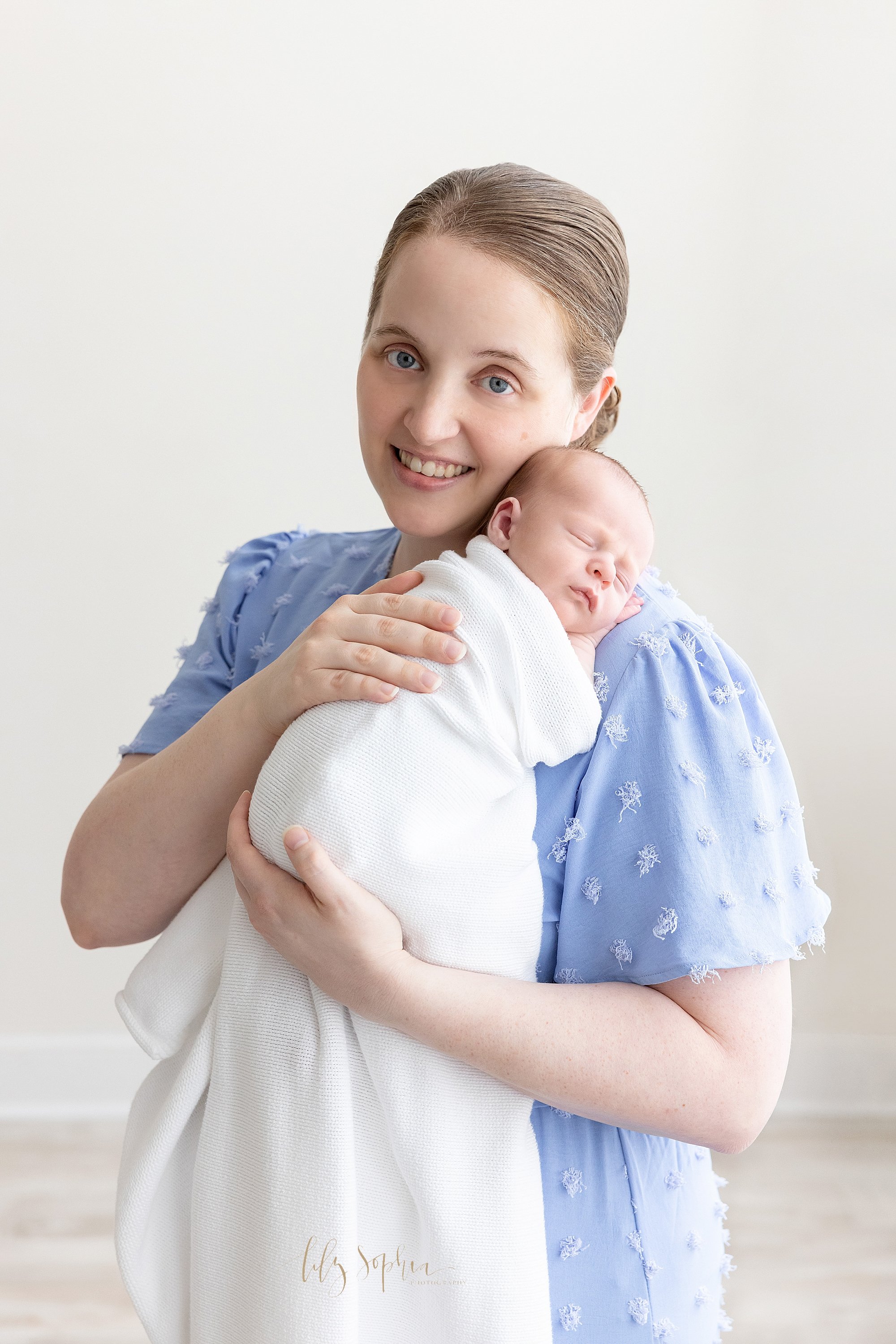  Newborn portrait of a mother holding her  peacefully sleeping newborn baby boy on his shoulder as she stands in a natural light studio near Cumming in Atlanta. 