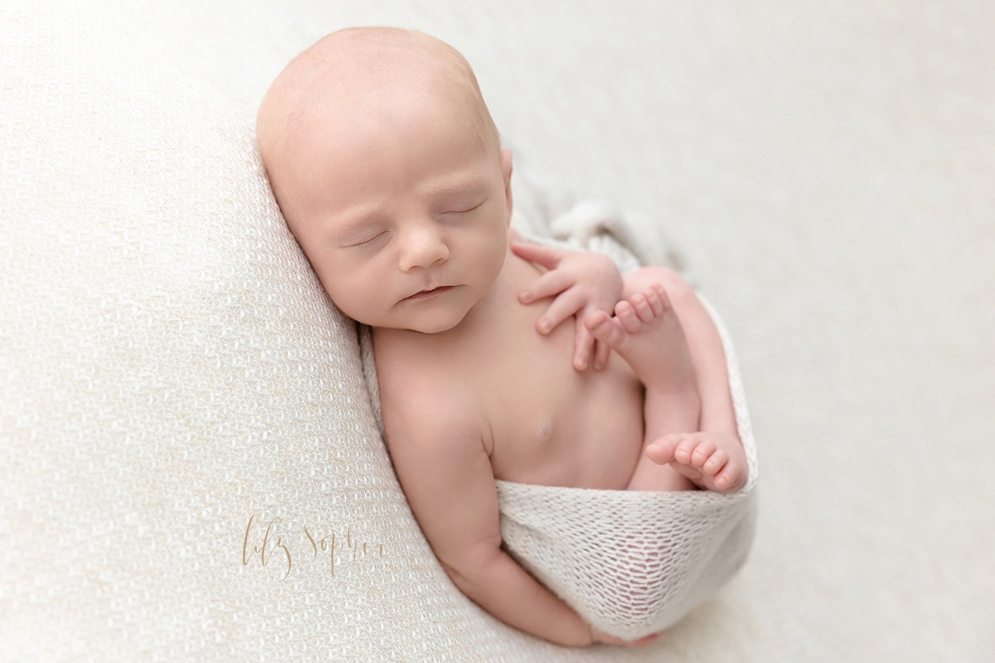  Newborn picture of a newborn baby boy as he is bundled in a soft white knitted blanket taken in natural light near Ansley Park in Atlanta in a photography studio. 