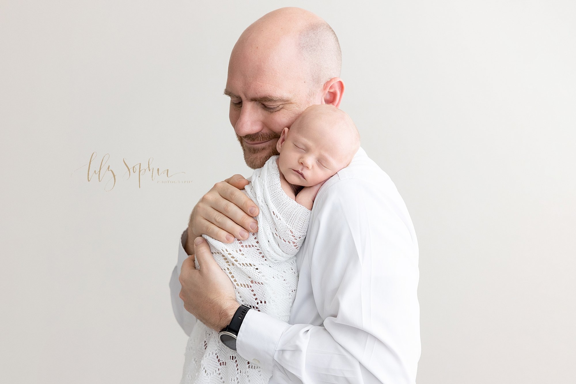 Newborn portrait of a father holding his sleeping newborn baby boy on his shoulder as the father treasures this time while standing in a photography studio near Kirkwood in Atlanta that uses natural light. 