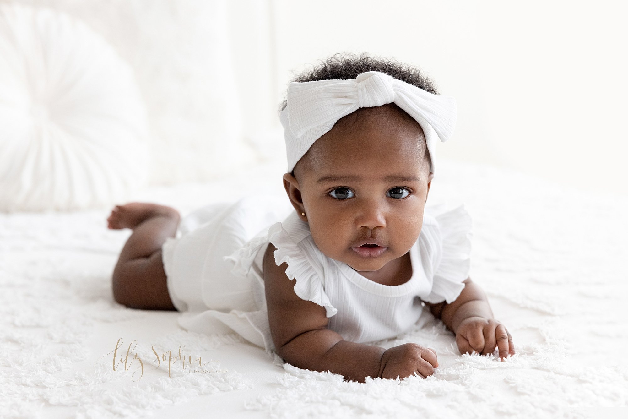  Baby photo shoot of an African-American baby girl as she lies on a bed in a natural light studio near Oakhurst in Atlanta. 
