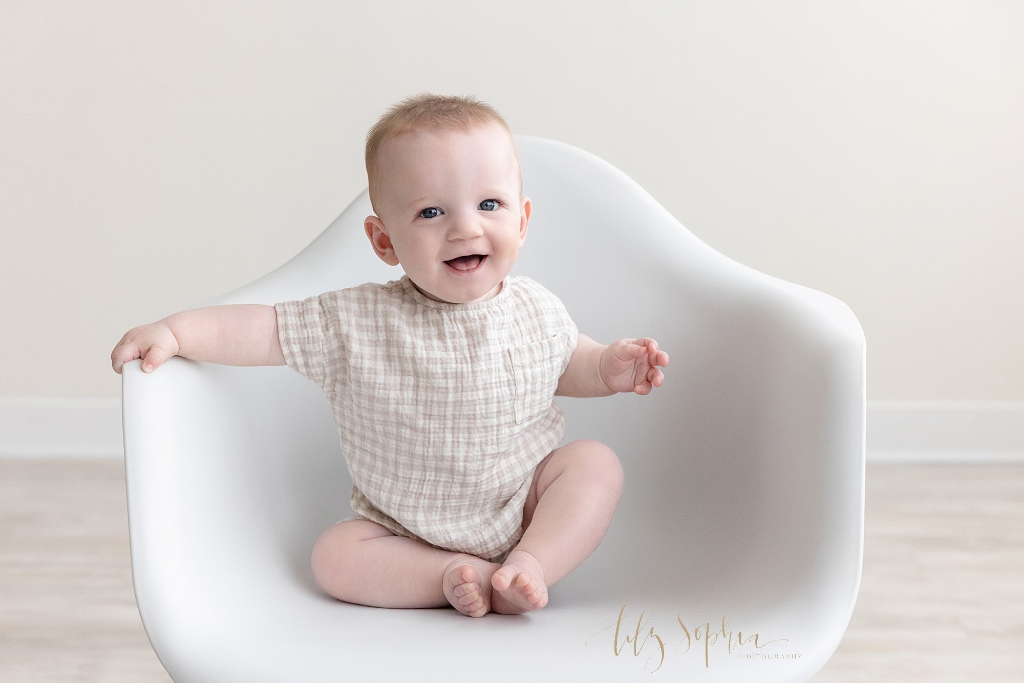  Baby photo of a happy baby boy sitting in a white molded chair in a natural light photography studio near Alpharetta in Atlanta. 