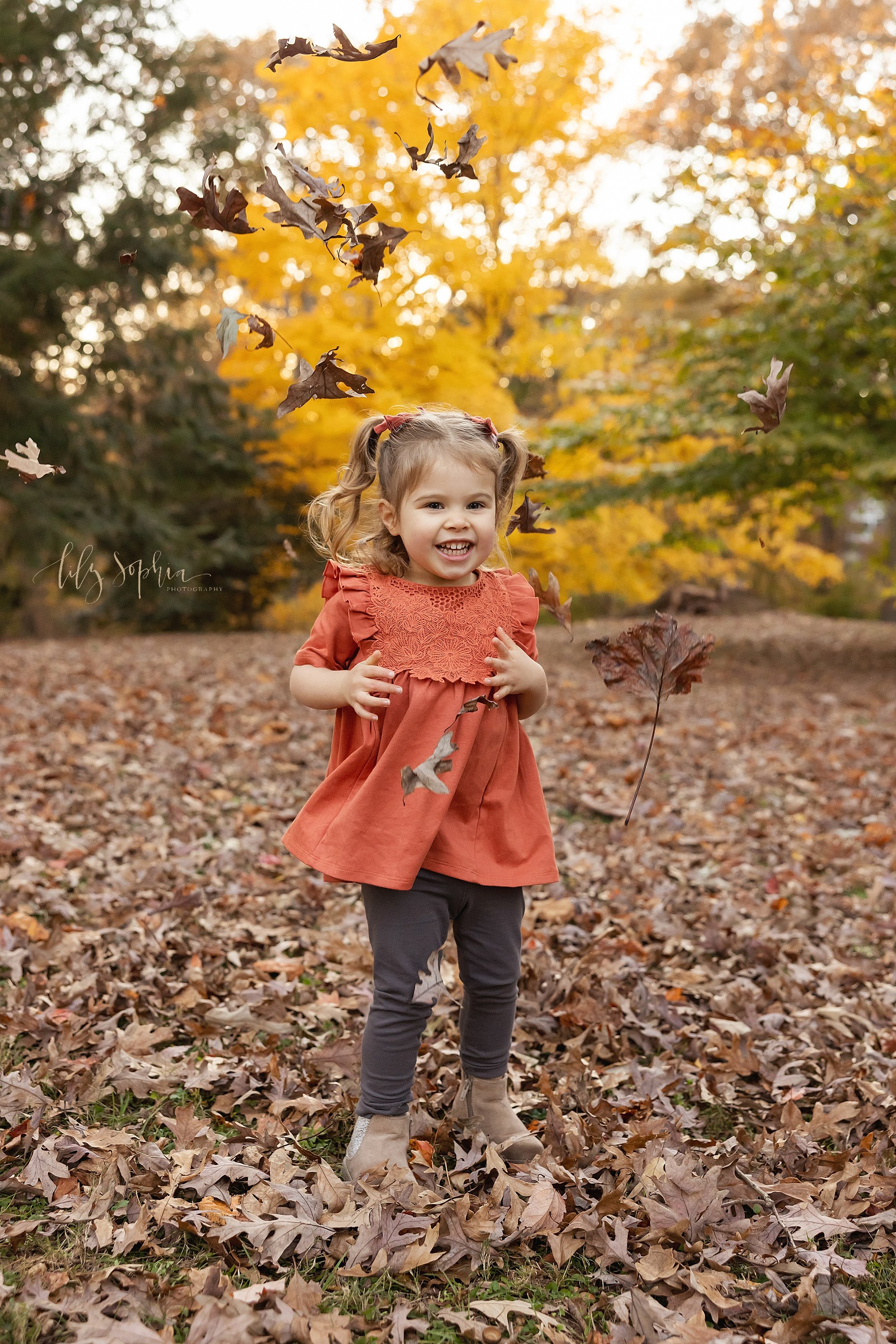  Family portrait of a little girl throwing leaves into the air in an Atlanta park during the fall season at sunset. 