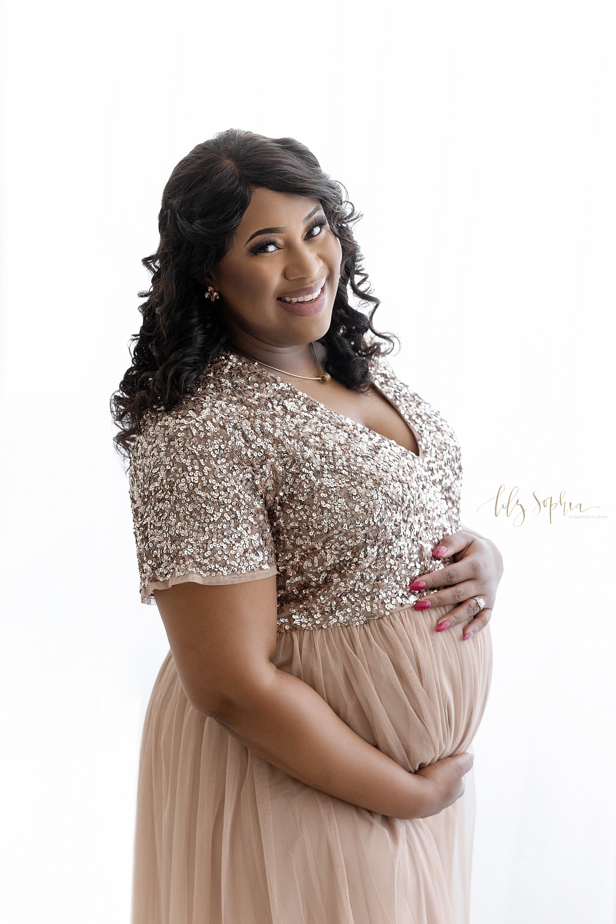  Maternity photo session of an African-American pregnant mother as she stands framing her belly in front of a window streaming natural light in a studio near Midtown in Atlanta, Georgia. 