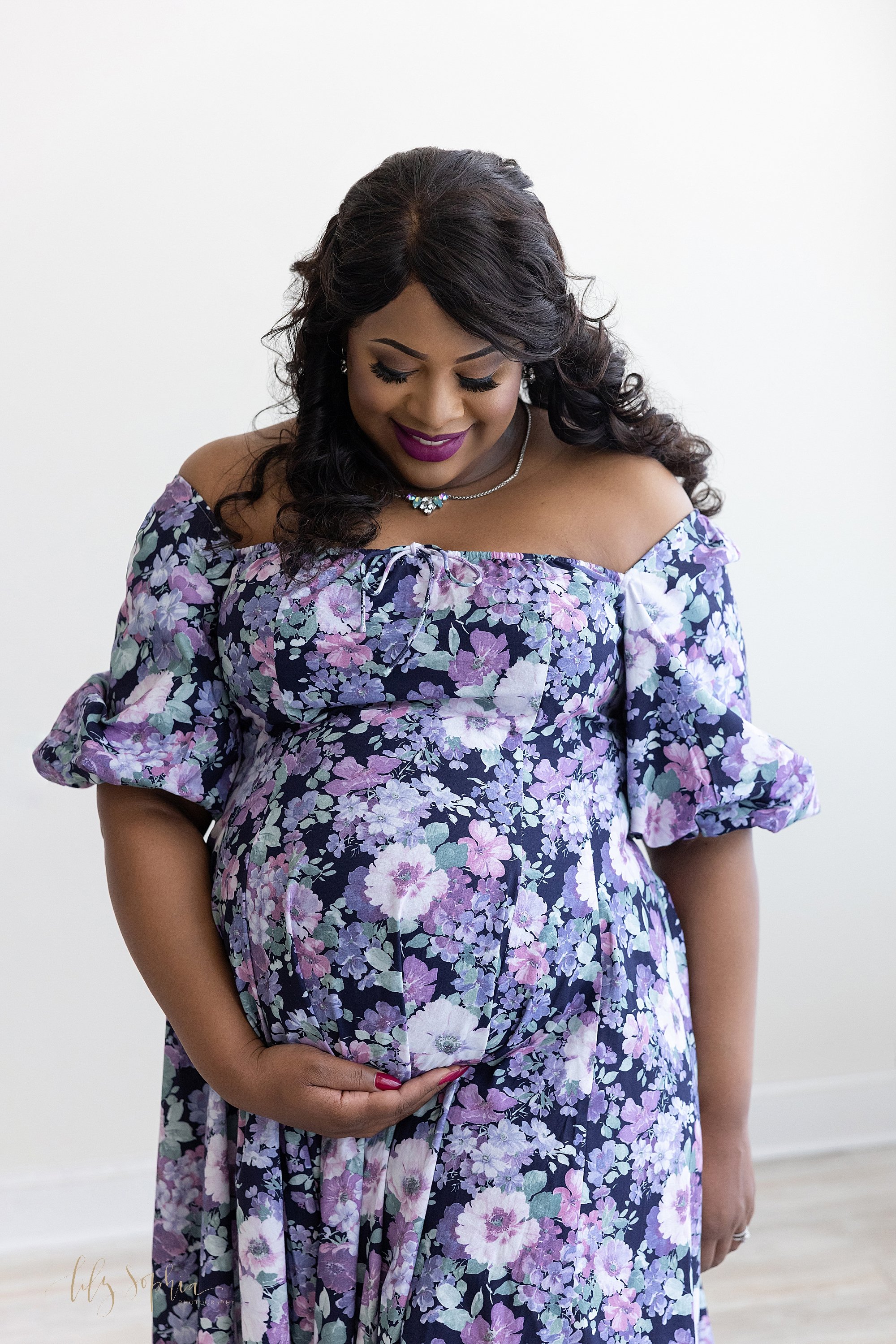  Maternity portrait of an African-American pregnant mother as she looks down at her child in utero and holds the base of her belly with her right hand taken near Alpharetta in Atlanta in a studio using natural light. 