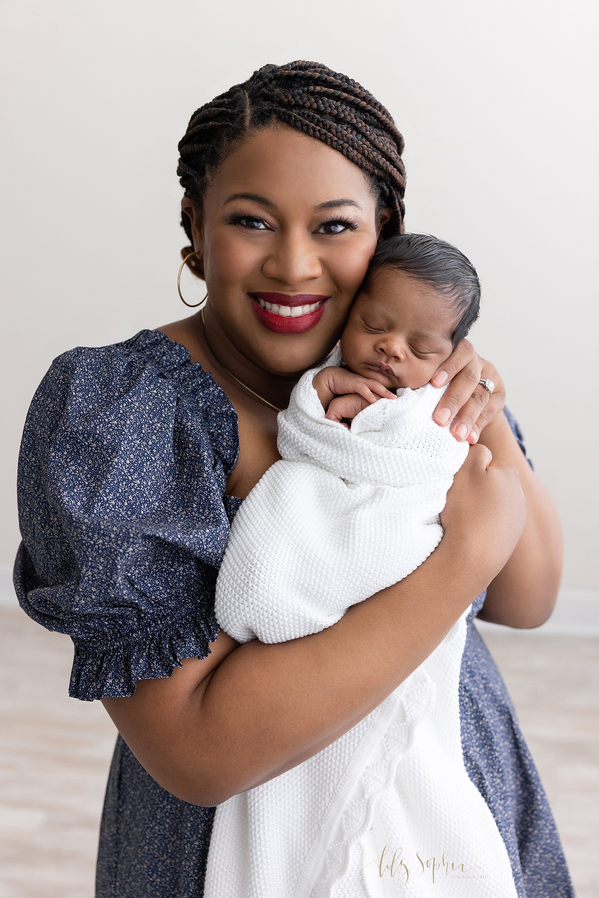  Newborn portrait of an African-American mother holding her peacefully sleeping newborn baby boy in front of her as they are cheek to cheek taken in a natural light studio near Morningside in Atlanta. 