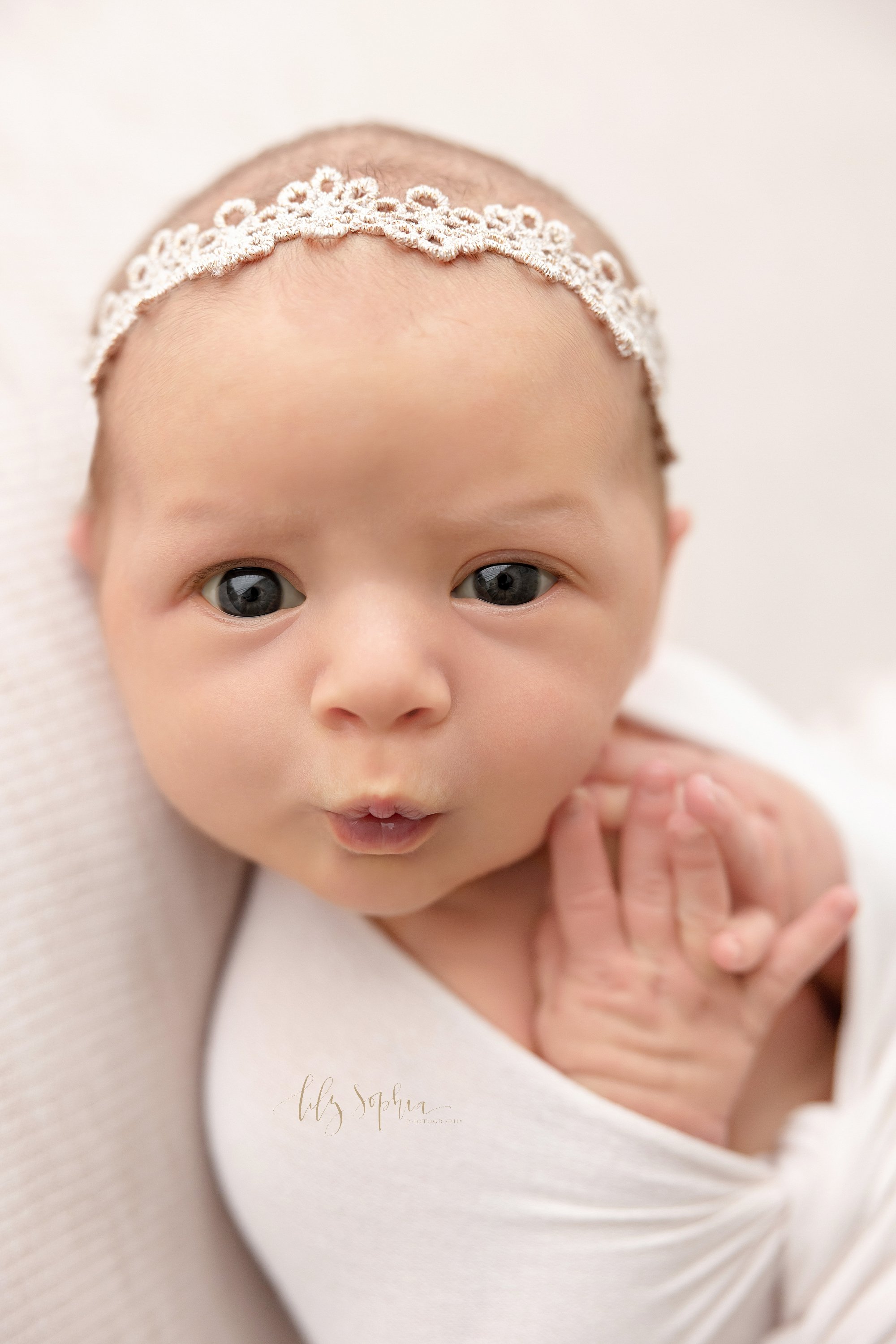  Newborn portrait of a wide awake newborn baby girl as she puckers her lips as if to whistle taken near Buckhead in Atlanta, Georgia in a natural light photography studio. 