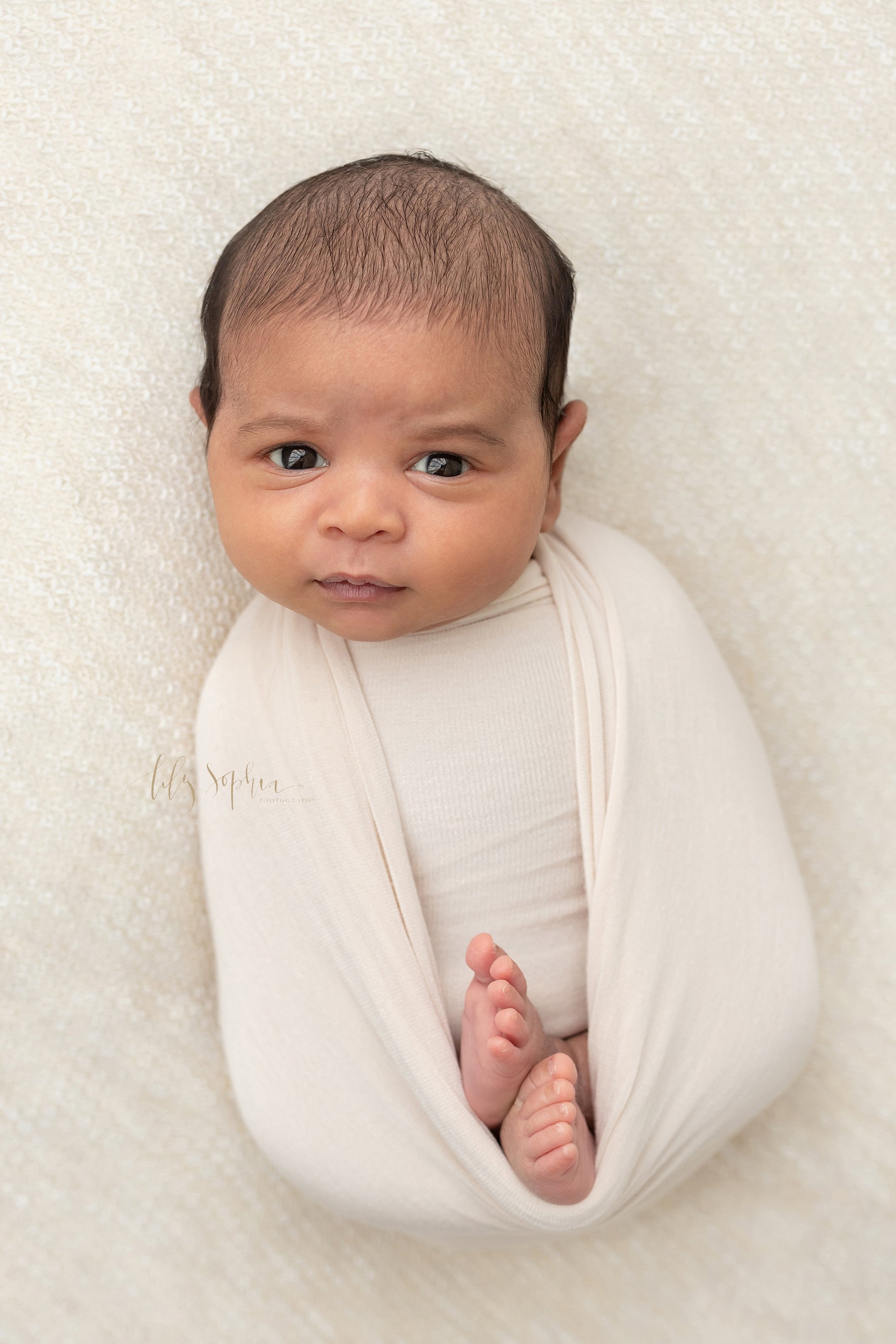  Newborn portrait of an Indian newborn baby boy as he lies on his back wrapped in a stretchy swaddle with his feet peeking out taken near Poncey Highlands in Atlanta in a natural light studio. 