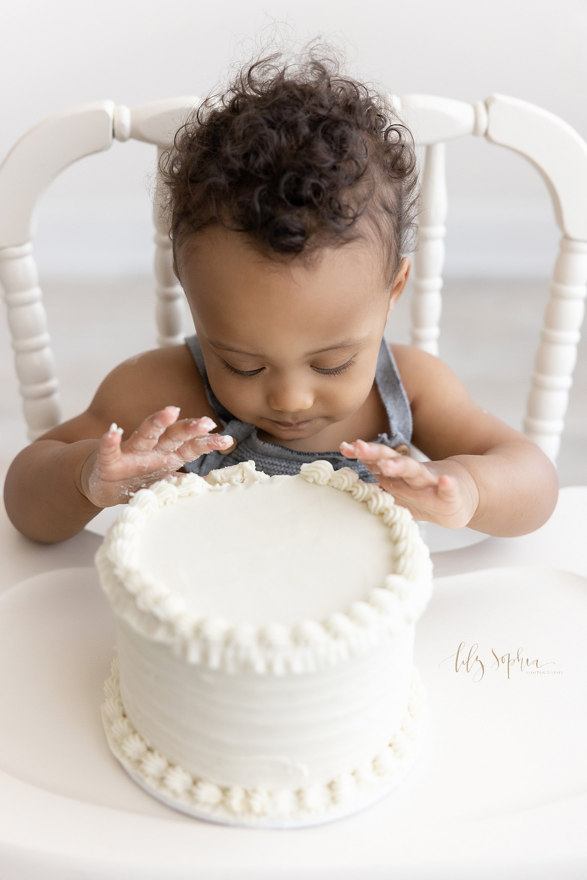  Overhead smash cake picture of an African-American little boy as he begins to pat his cake with his hands taken in natural light in a studio near Vinings in Atlanta, Georgia. 