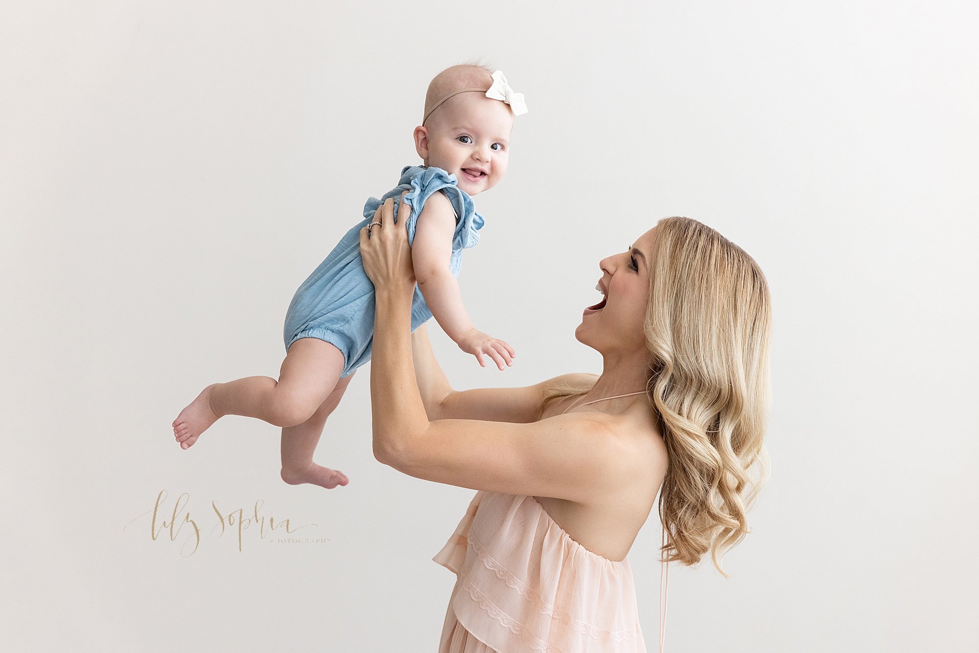  Family photo of a mother holding her baby daughter above her head as she stands in a natural light studio near Kirkwood in Atlanta. 