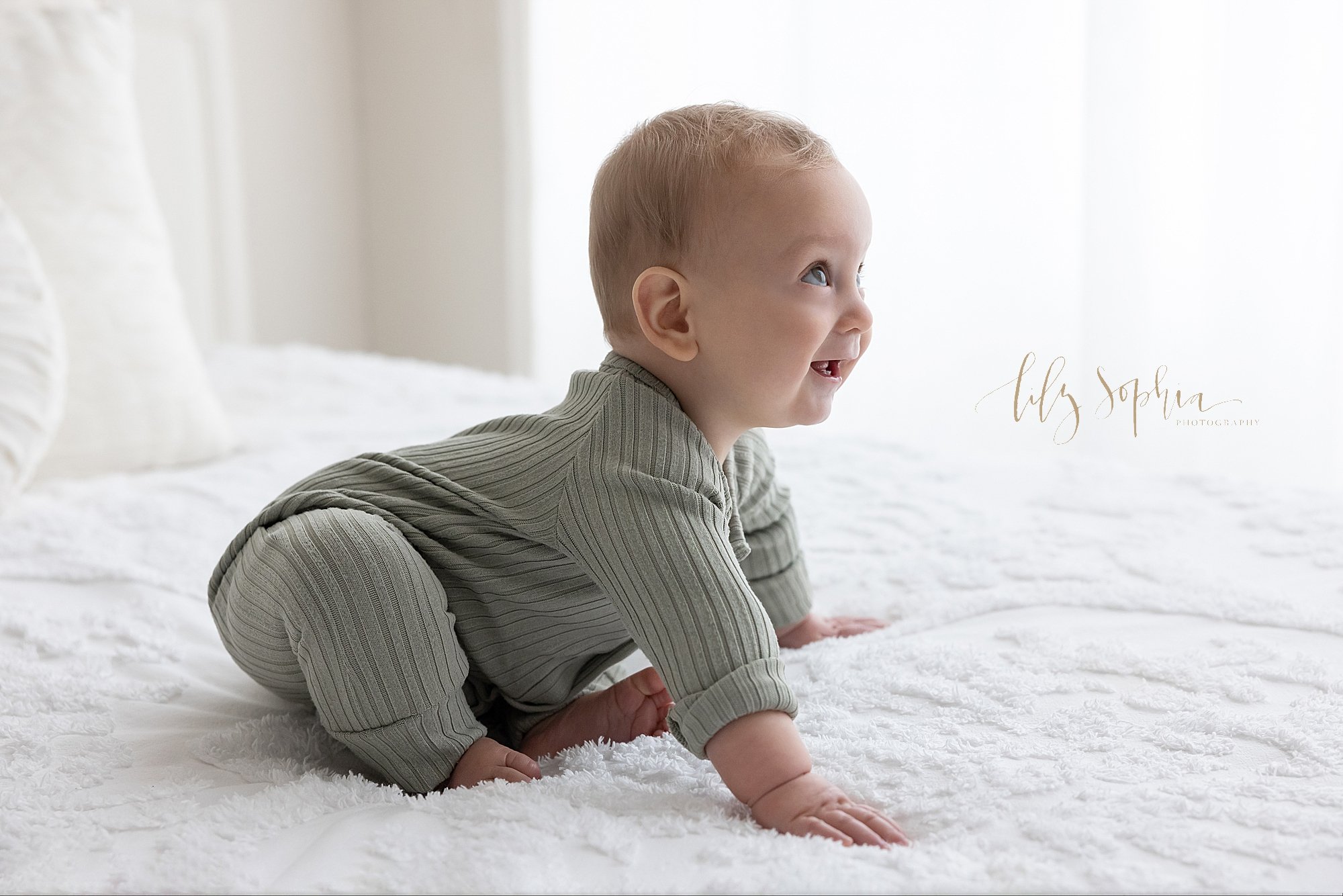  Baby photo of a baby boy as he begins to crawl across a bed in front of a window streaming natural light in a photography studio located near Cumming in Atlanta Georgia. 