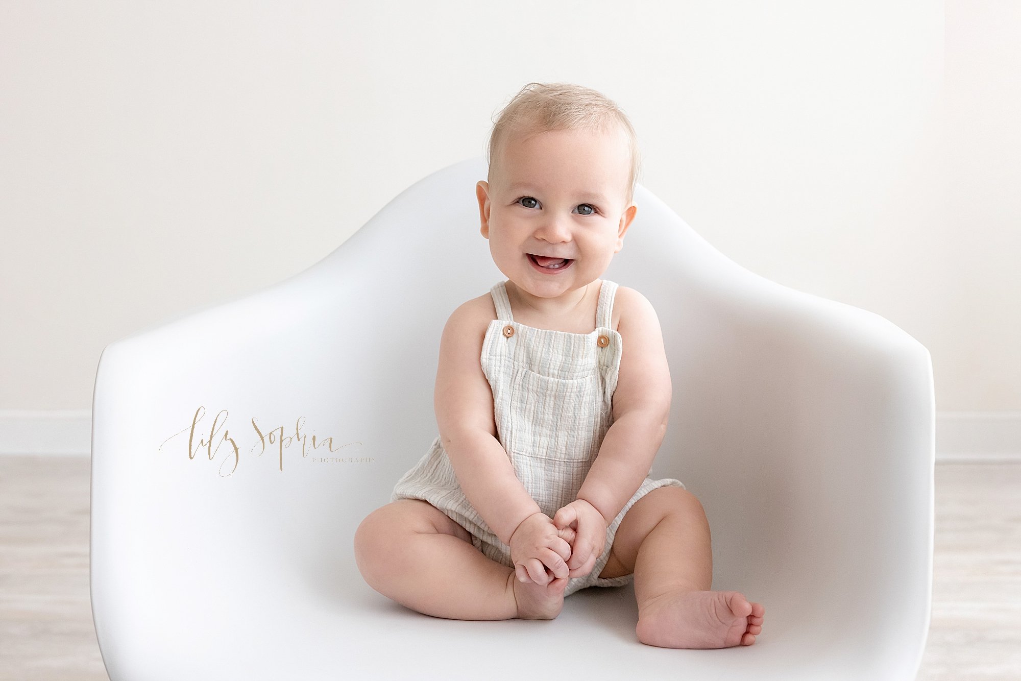  Milestone photo of a smiling baby boy as he sits in a molded chair all by himself taken in a natural light studio near Midtown in Atlanta. 