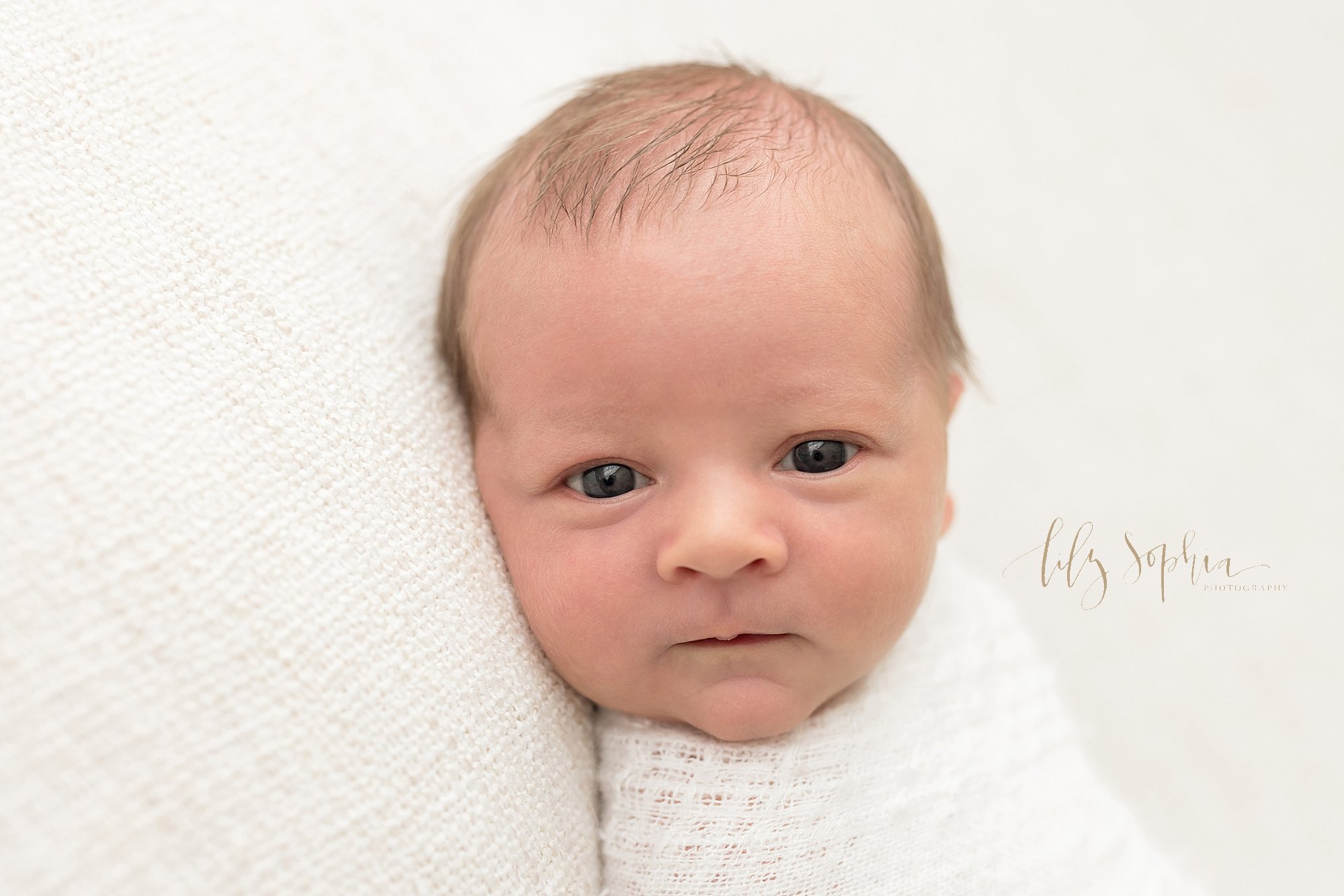  Newborn portrait of a wide awake newborn baby boy swaddled to his neck in a crocheted white blanket as he looks over his right shoulder taken in a natural light studio near Sandy Springs in Atlanta. 