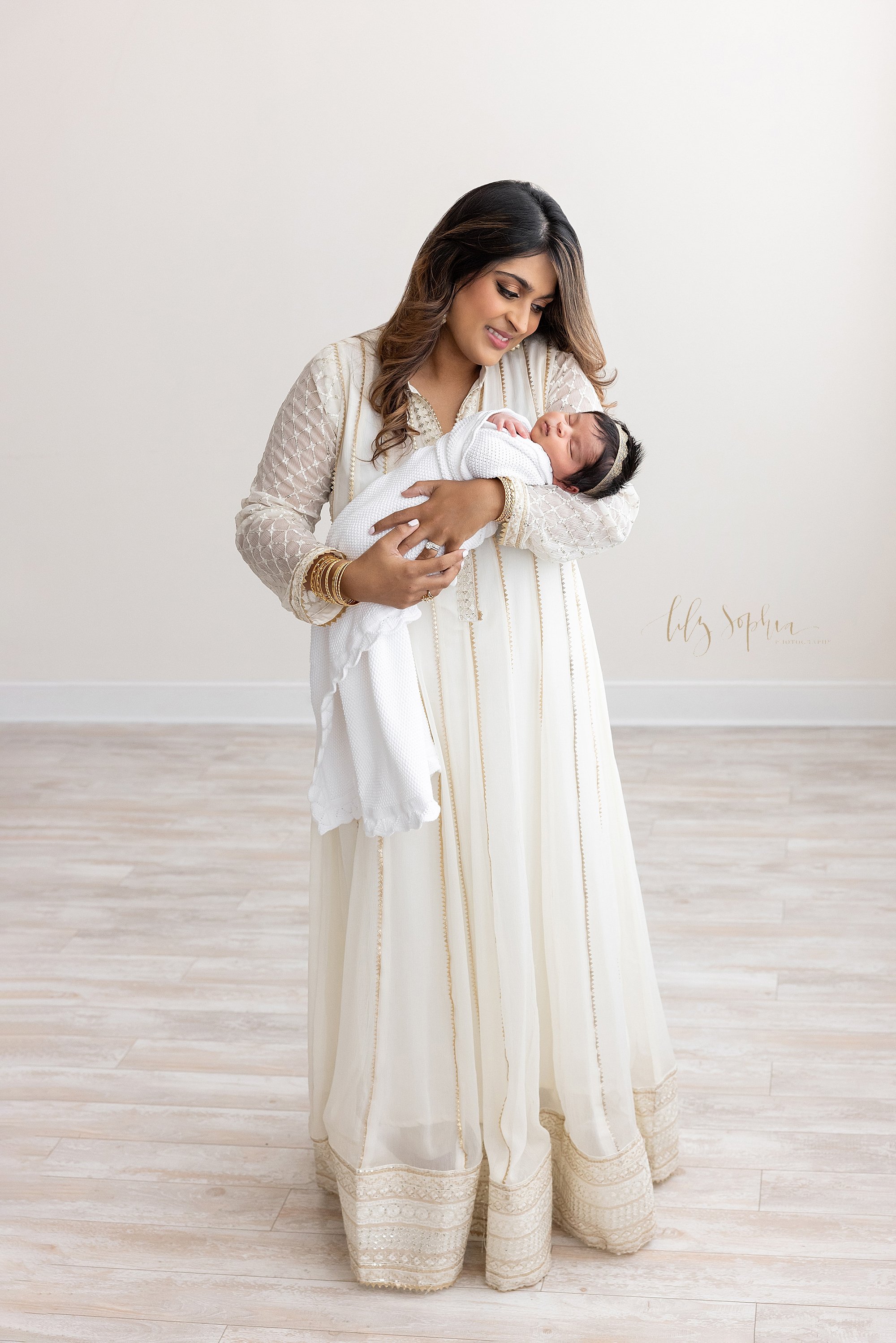  Newborn photo session with a mother holding her newborn baby girl in her arms as she stands and admires her daughter in a natural light studio near Decatur in Atlanta, Georgia. 