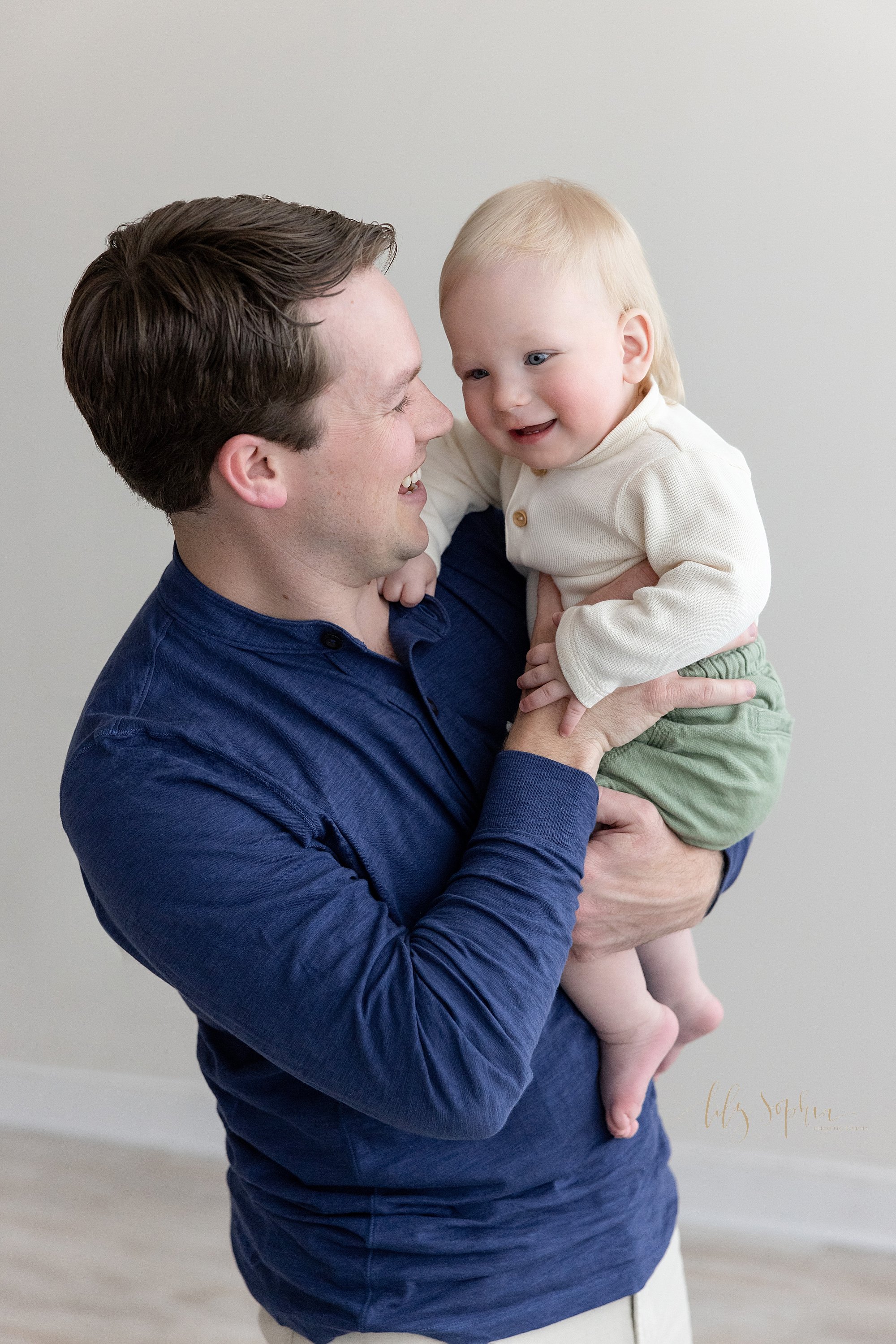  Family photo of a father holding his one year old son for a first birthday photo session in a photography studio near Roswell in Atlanta that uses natural light. 