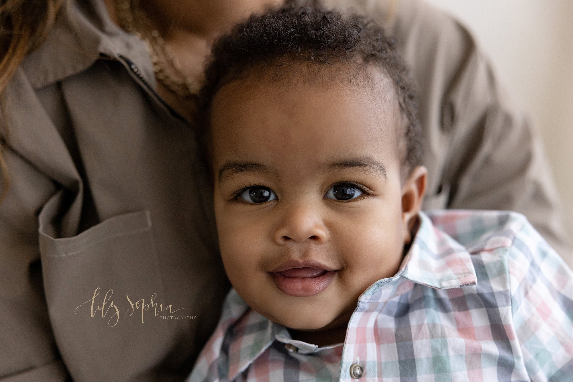  First birthday portrait of a one year old African-American boy as he is held on his mother’s lap taken in a natural light studio near Midtown in Atlanta, Georgia. 