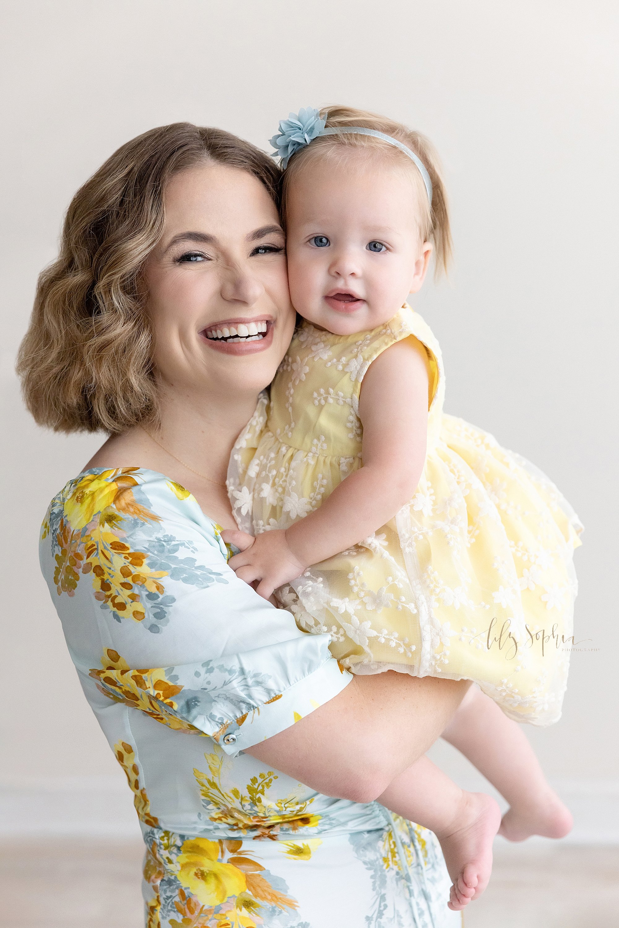 Family mother and daughter portrait of a mother holding her one year old baby girl in her arms so their heads can be cheek to cheek taken near Decatur in Atlanta in a photography studio that uses natural light. 