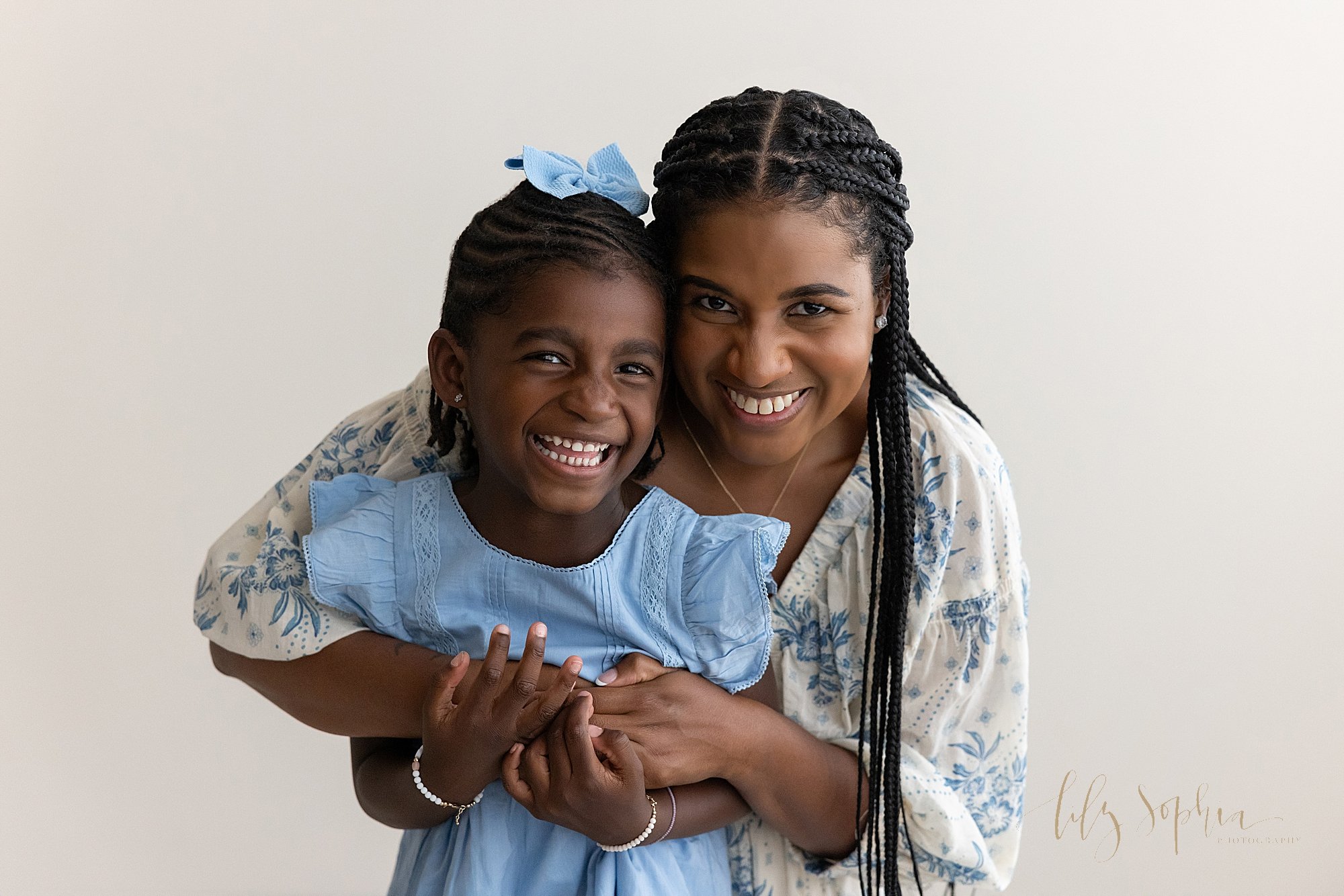  Family picture of an African-American mother as she grabs her daughter from behind and the two of them smile while standing in a studio that uses natural light near Poncey Highlands in Atlanta. 