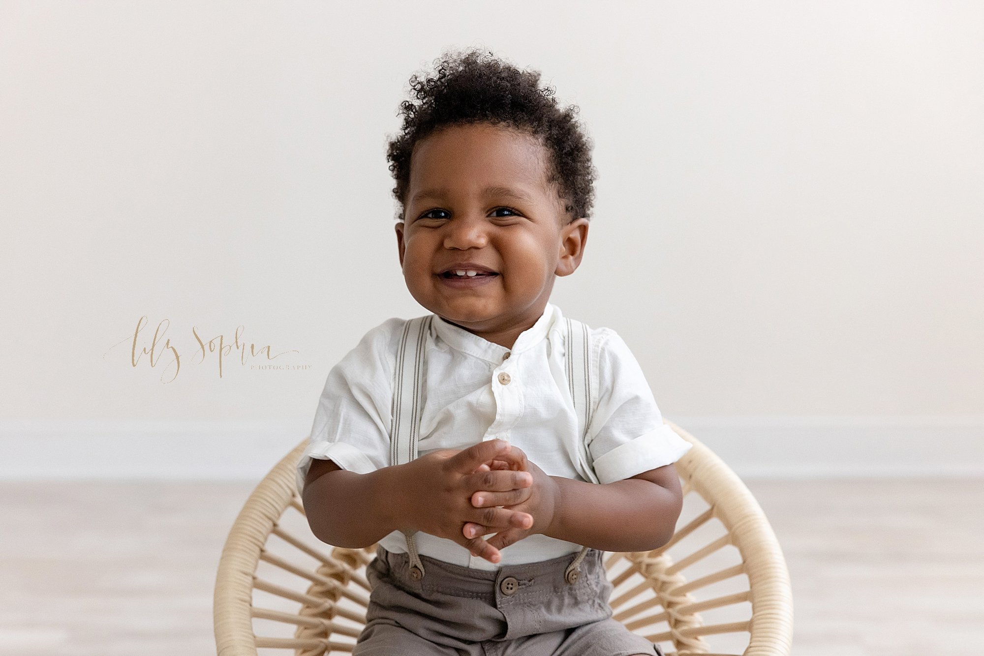  Family photo session of an African-American toddler boy as he sits in a bamboo chair in a natural light photography studio near Vinings in Atlanta, Georgia. 