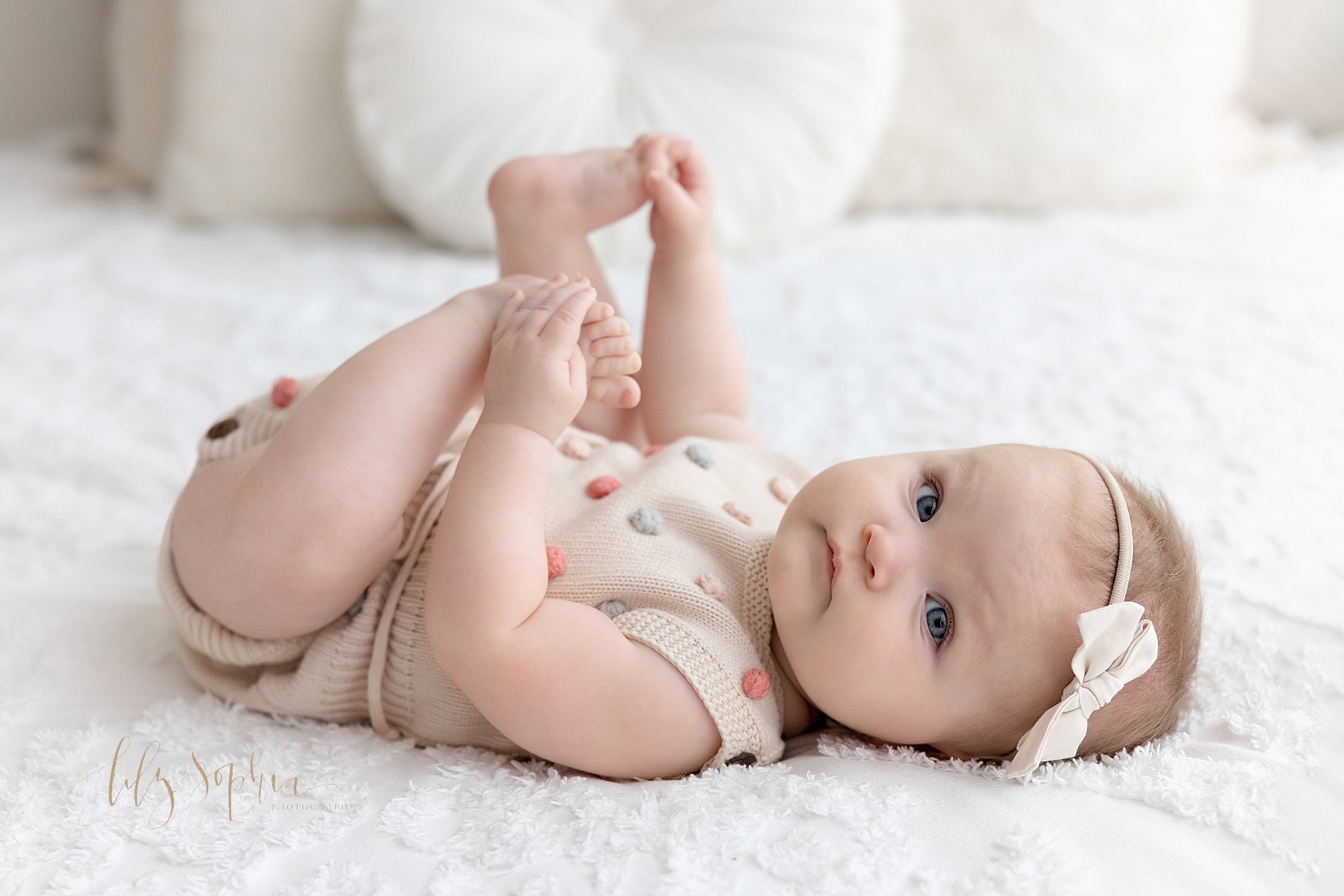  Baby portrait of a baby girl lying on her back on a bed and playing with her feet taken near Ansley Park in Atlanta in a photography studio using natural light. 