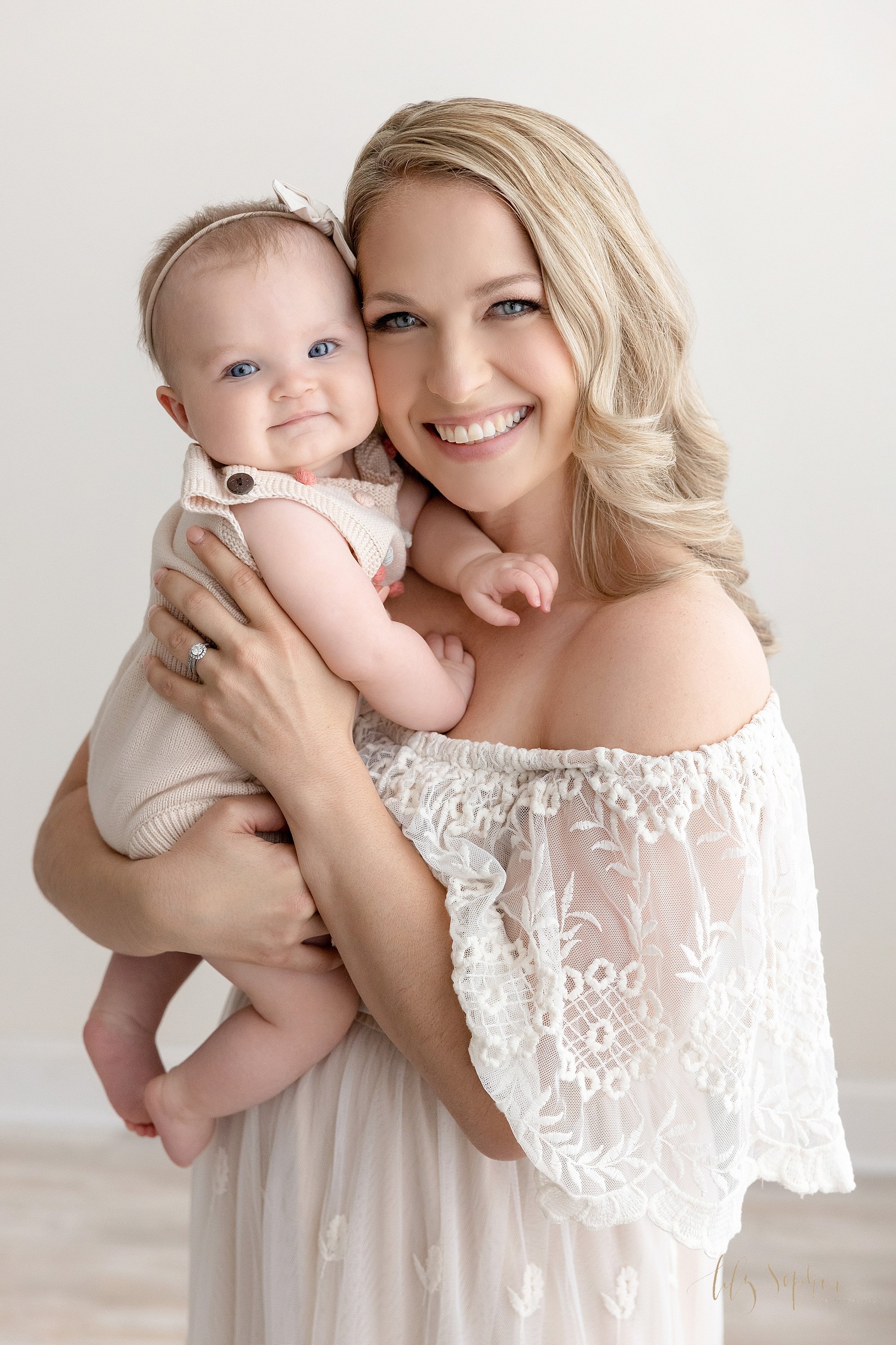  Baby portrait with mom holding her baby girl with their faces cheek to cheek while standing in a photography studio near Oakhurst in Atlanta that uses natural light. 