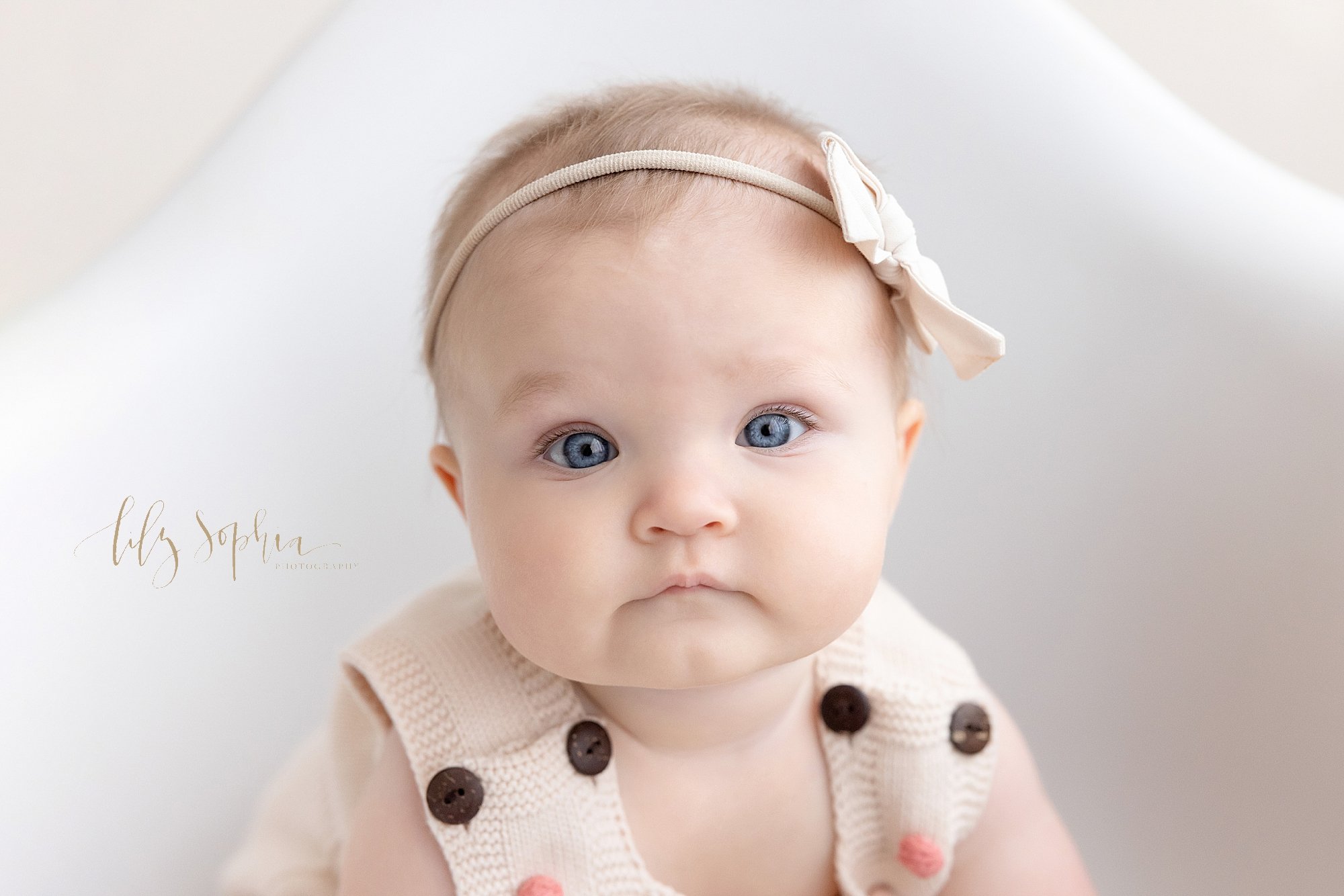  Close-up baby portrait of a baby girl sitting in a white molded chair taken near Virginia Highlands in Atlanta in a studio using natural light. 