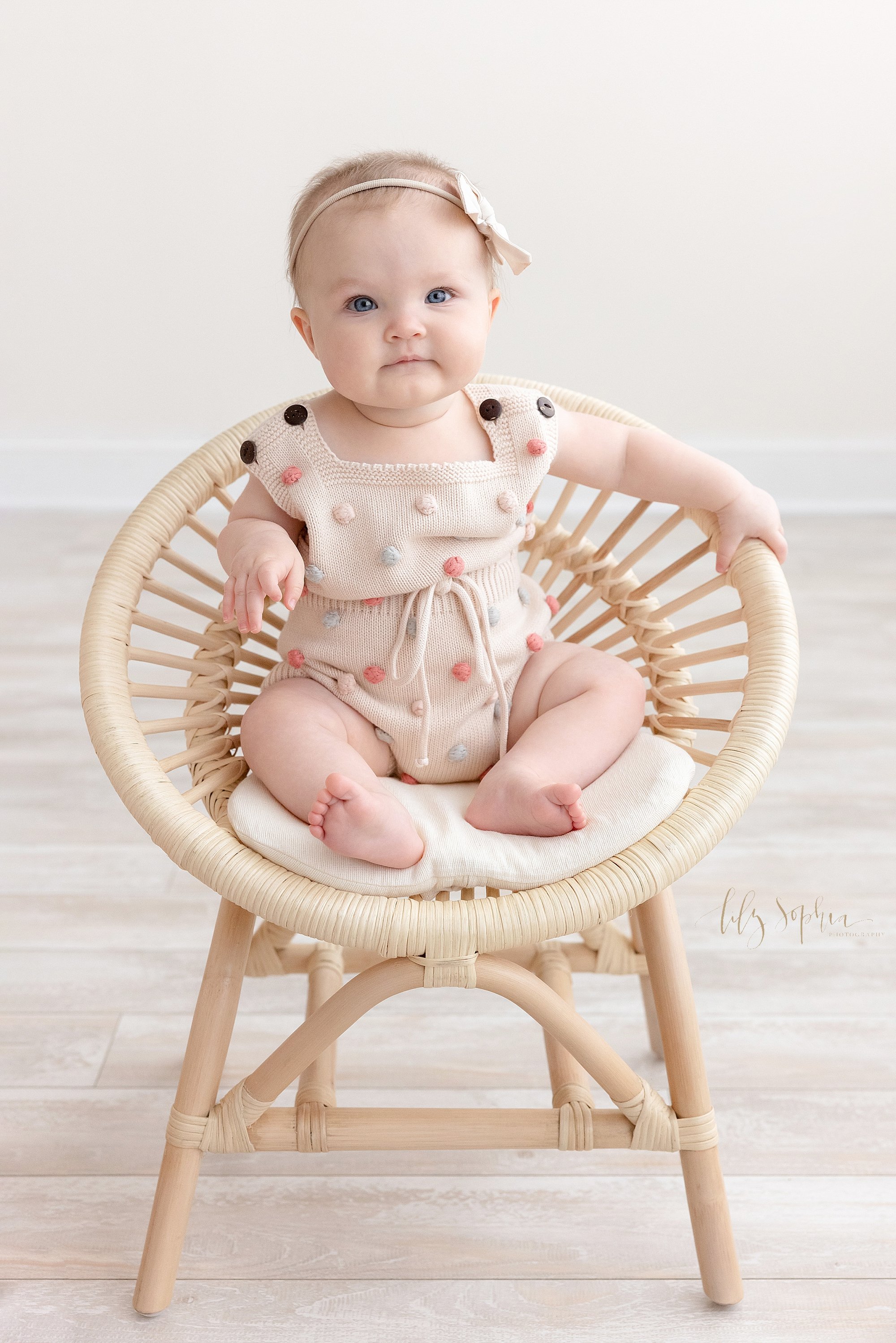  Baby sitting milestone photo of a baby girl sitting in a bamboo chair in a natural light studio near Poncey Highlands in Atlanta. 