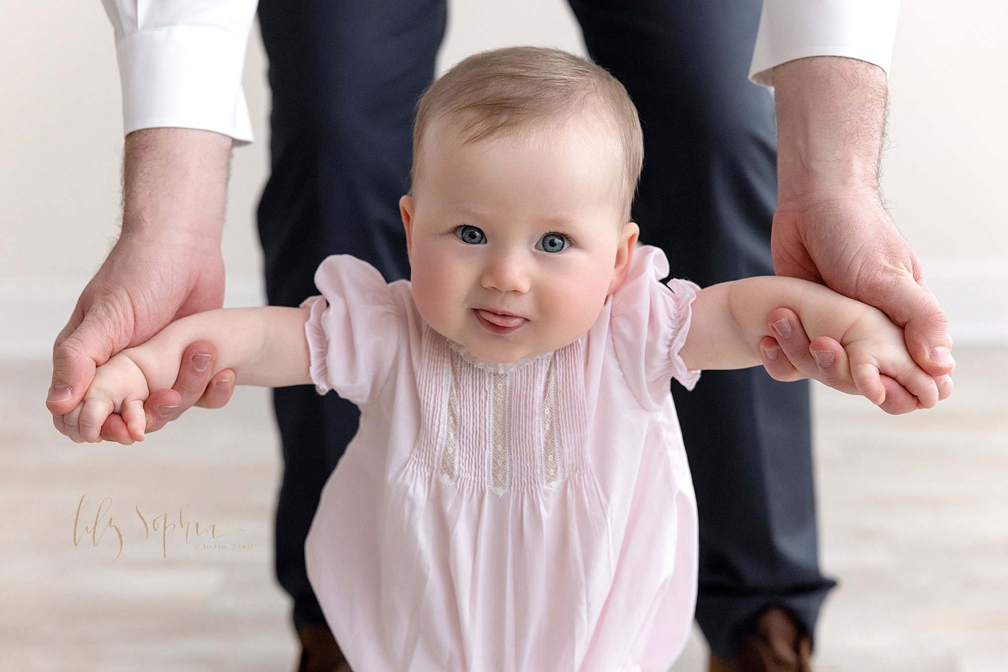  Baby portrait of a baby girl as she holds on to her fathers hands and walks in front of her father in a studio using natural light taken near Ansley Park in Atlanta, Georgia. 